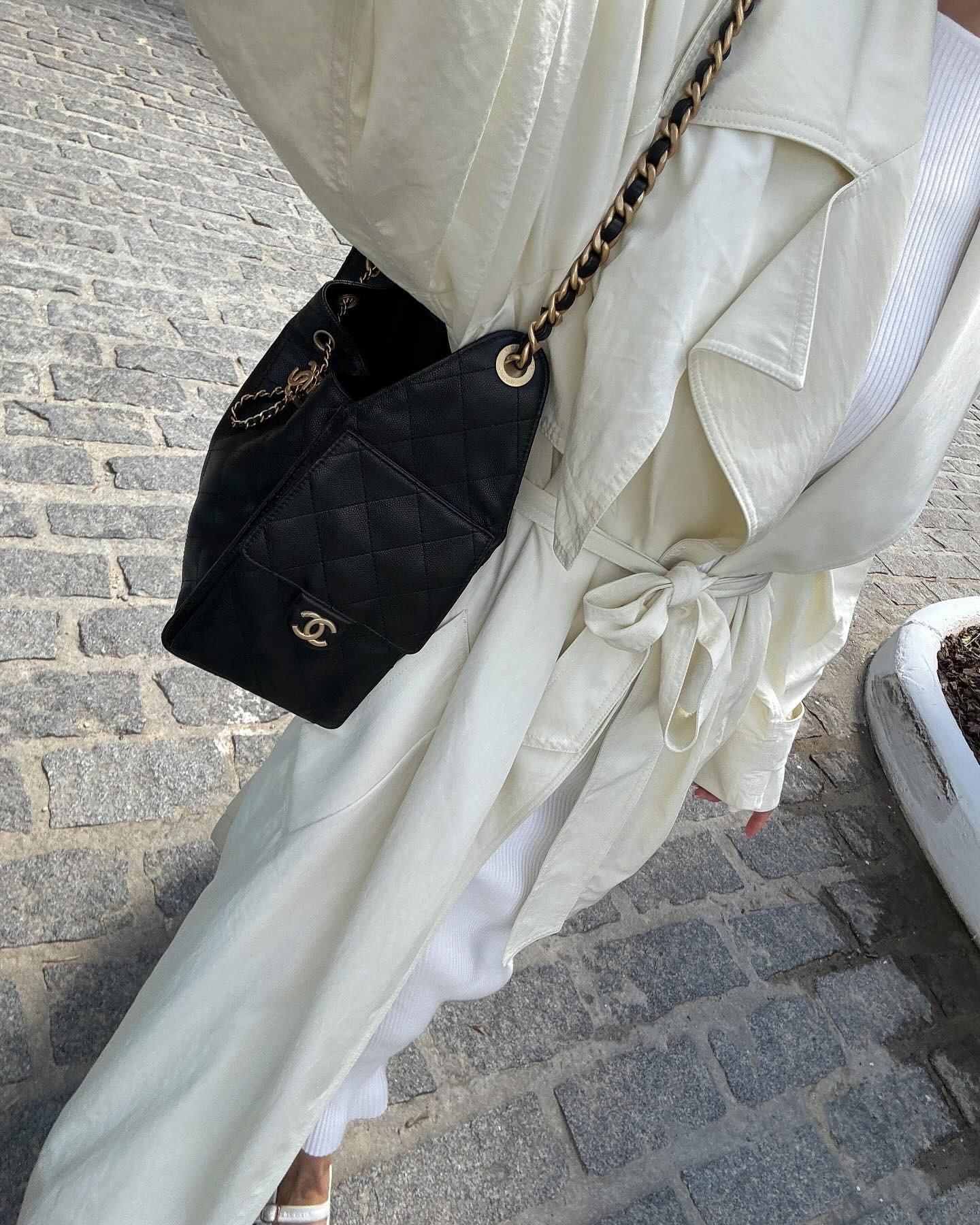 Influencer @rikkekrefting wears a Chanel 25 handbag with a white long-line trench coat and white jeans.