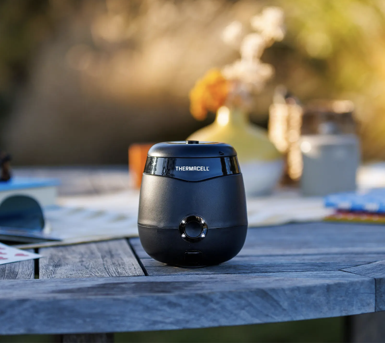 Thermacell mosquito repeller, a small black semi-circular unit, sitting on a picnic table.