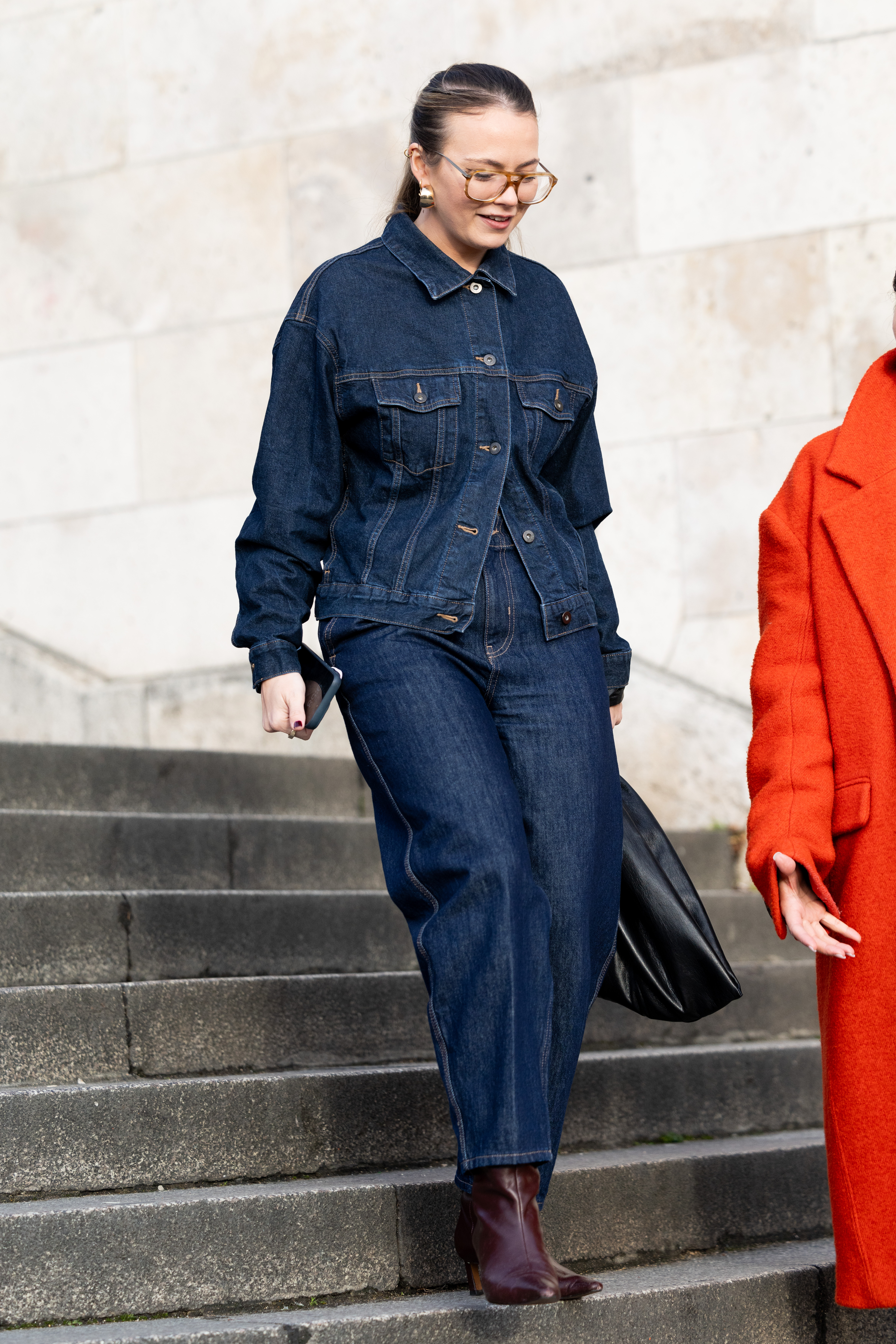 A woman wearing a matching dark wash denim jacket and jeans with burgundy boots