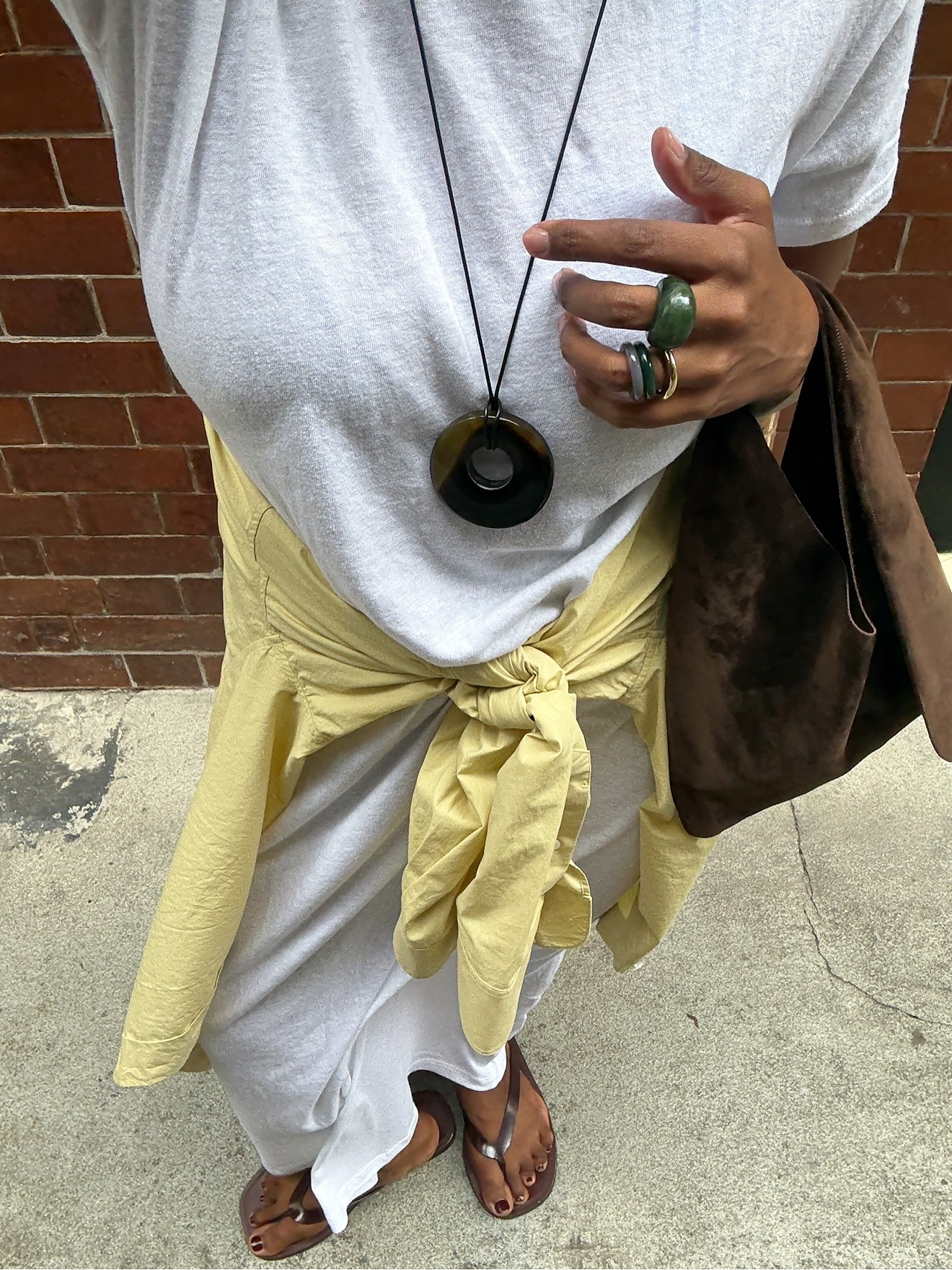 A woman taking an outfit picture wearing brown flip flips with a chocolate brown pedicure