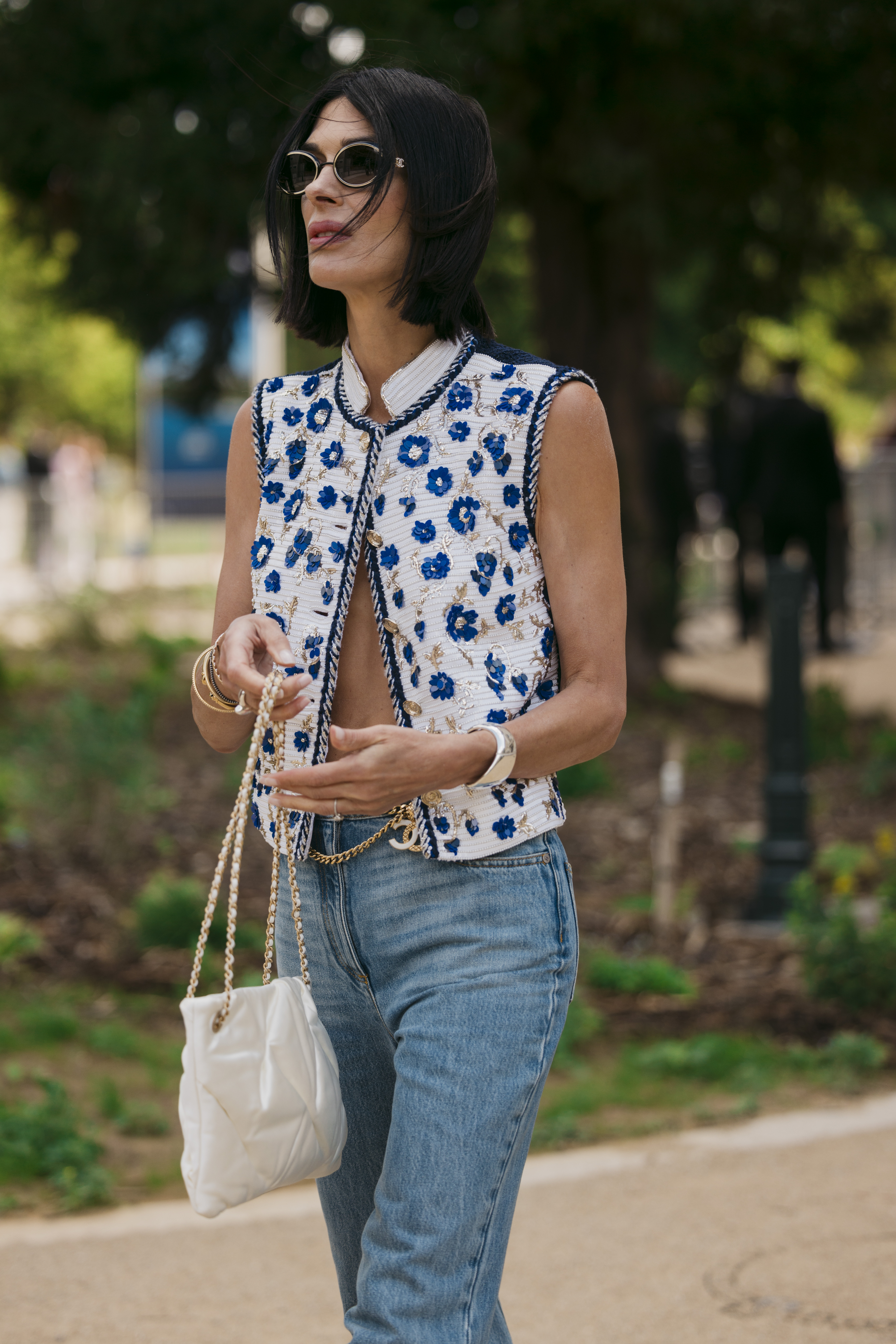 Guest wearing a Chanel vest, jeans, and a white Chanel bag to FW24 Chanel Haute Couture show in Paris.