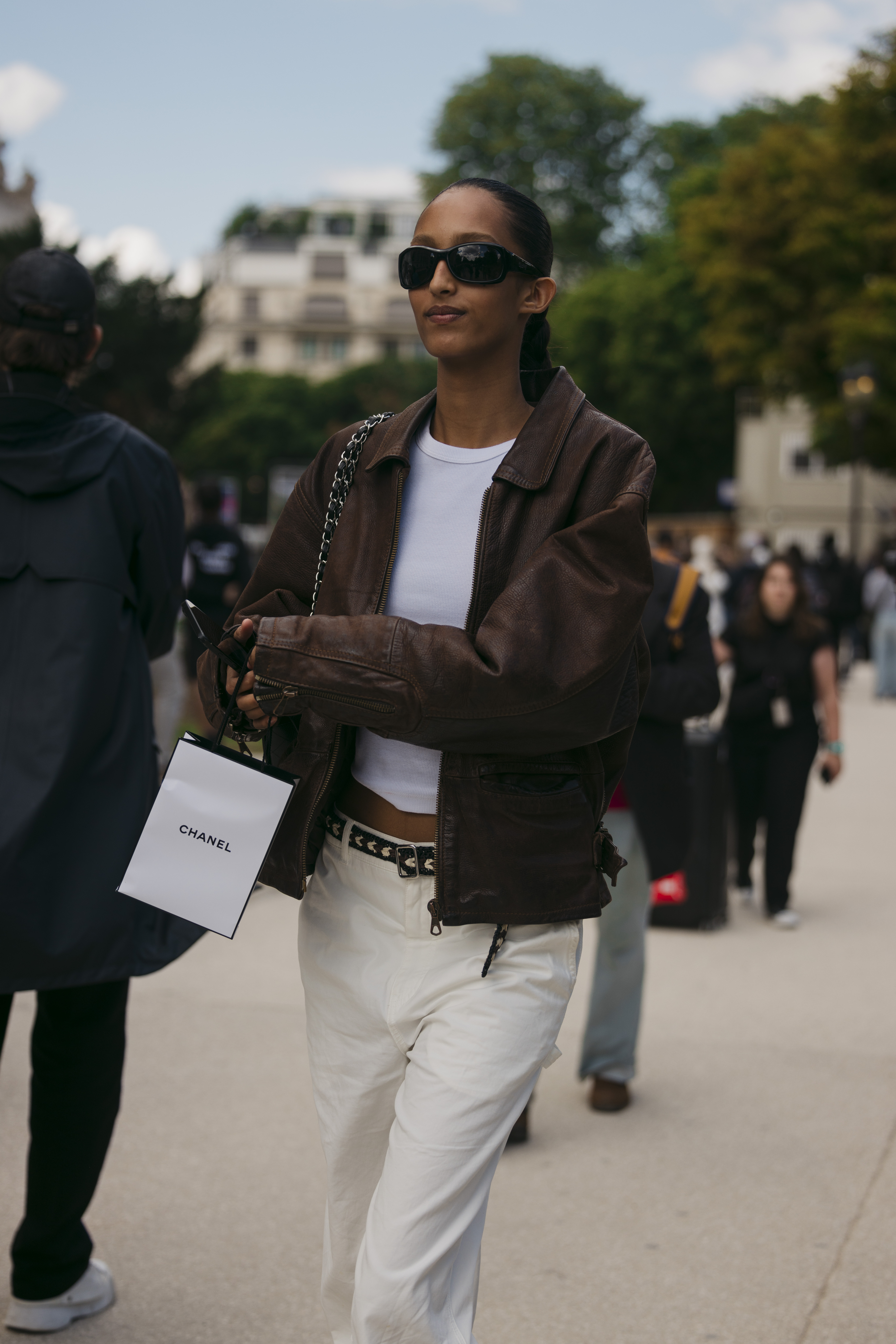 Mona Tougaard outside of Chanel wearing a brown suede jacket, a white T-shirt, and white jeans.
