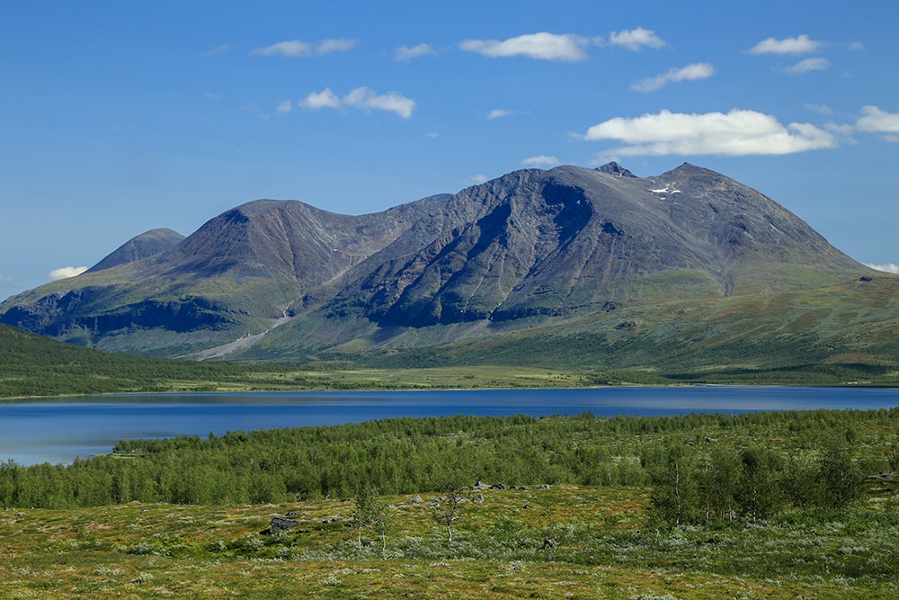 A wide view of hulking mountains above forests and a lake