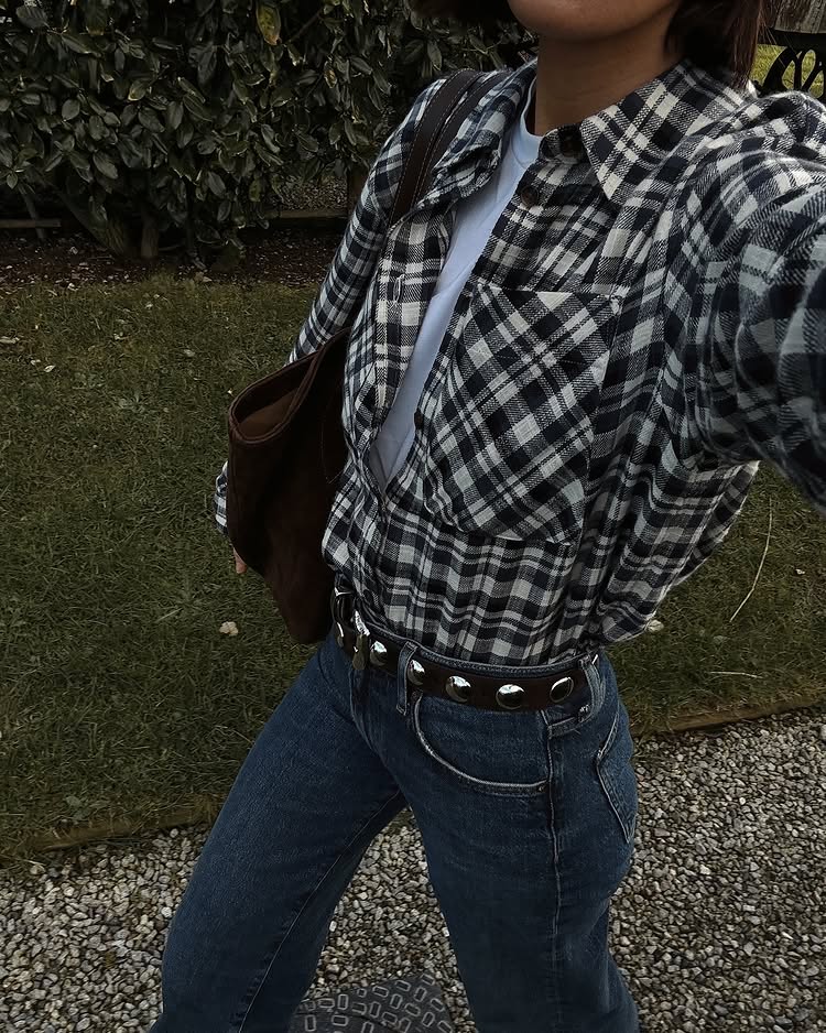 @_jessicaskye wears a black and white checked shirt tucked into dark blue jeans and finished with Khaite's studded Benny belt