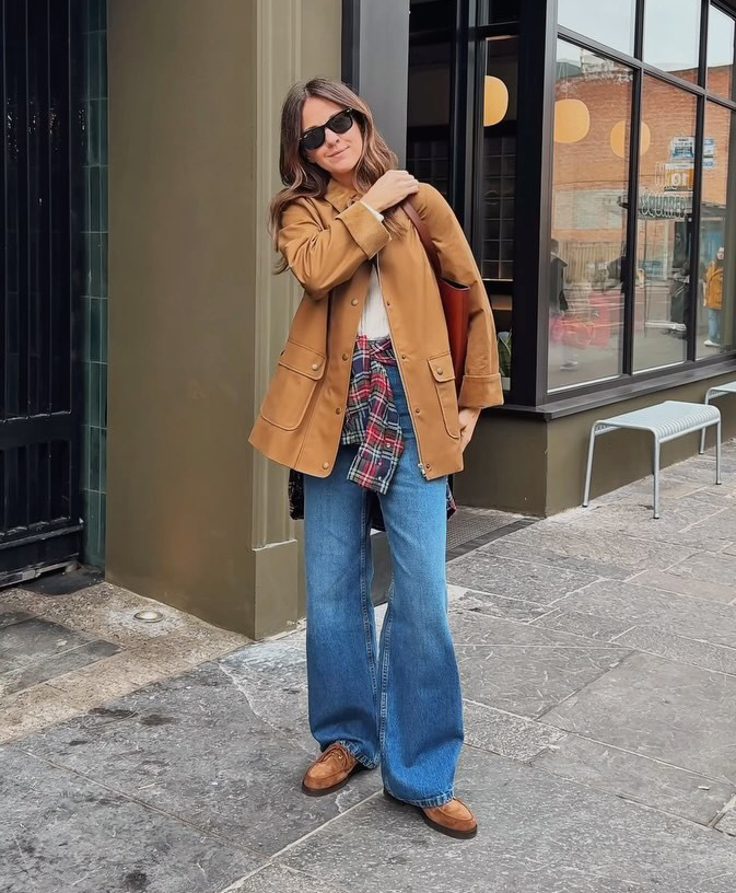@kimturkington_ wears a tan suede jacket, blue flared jeans and a red and navy shirt tied around the waist