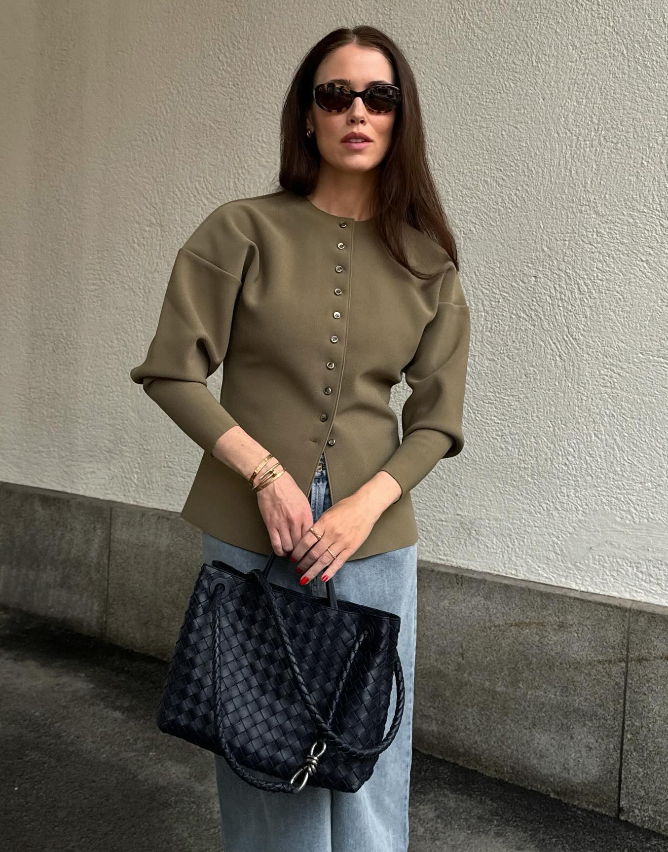 @annabelrosendahl wears an olive green waisted cardigan with blue jeans and a black woven Bottega Veneta leather bag