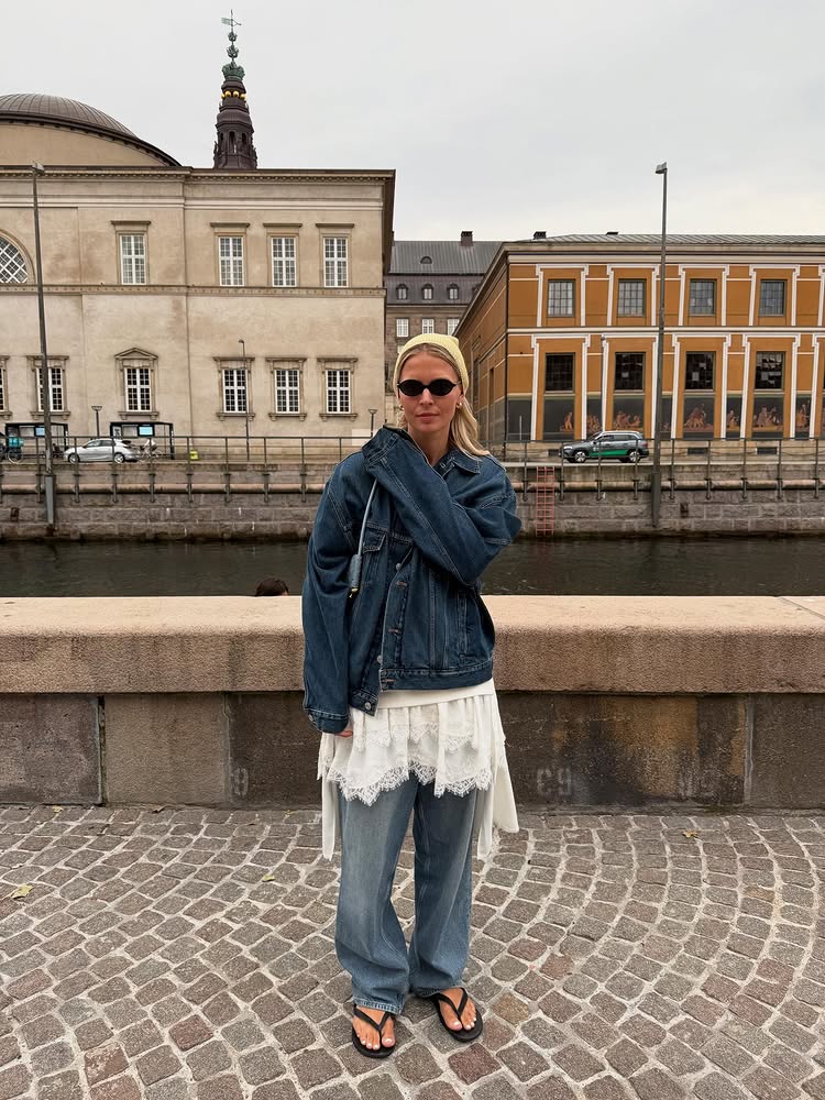 @holliemercedes wears a denim jacket, cream lace minidress, baggy jeans and flip-flops
