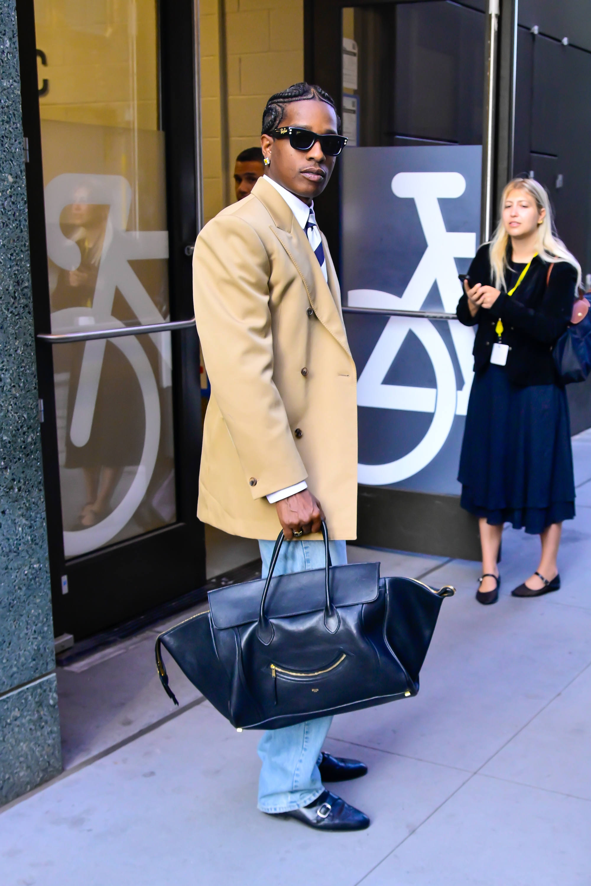 ASAP Rocky wears a camel blazer, black Celine Luggage Smile bag, jeans, and black loafers.