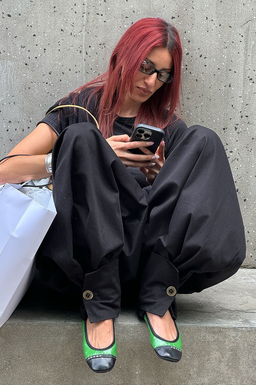 A woman wearing a black T-shirt, black button hem pants, and green flats.