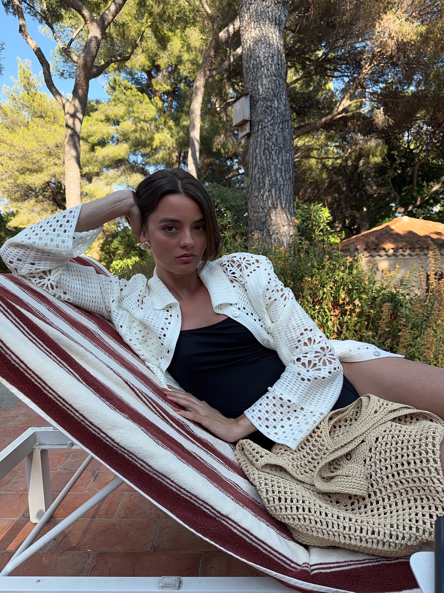 Influencer @maryljean wears a crochet cardigan over a black swimsuit with a crochet handbag.