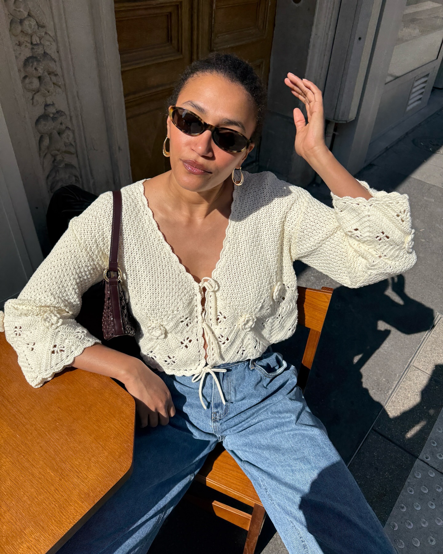 Influencer @lenafarl wears a crochet cardigan with blue jeans and a chocolate brown leather handbag.