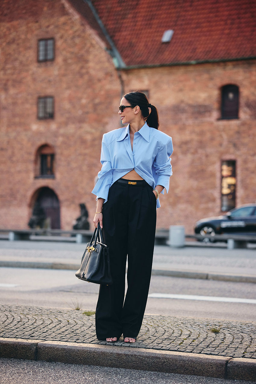 A woman wearing a blue button down shirt and black pants with sandals