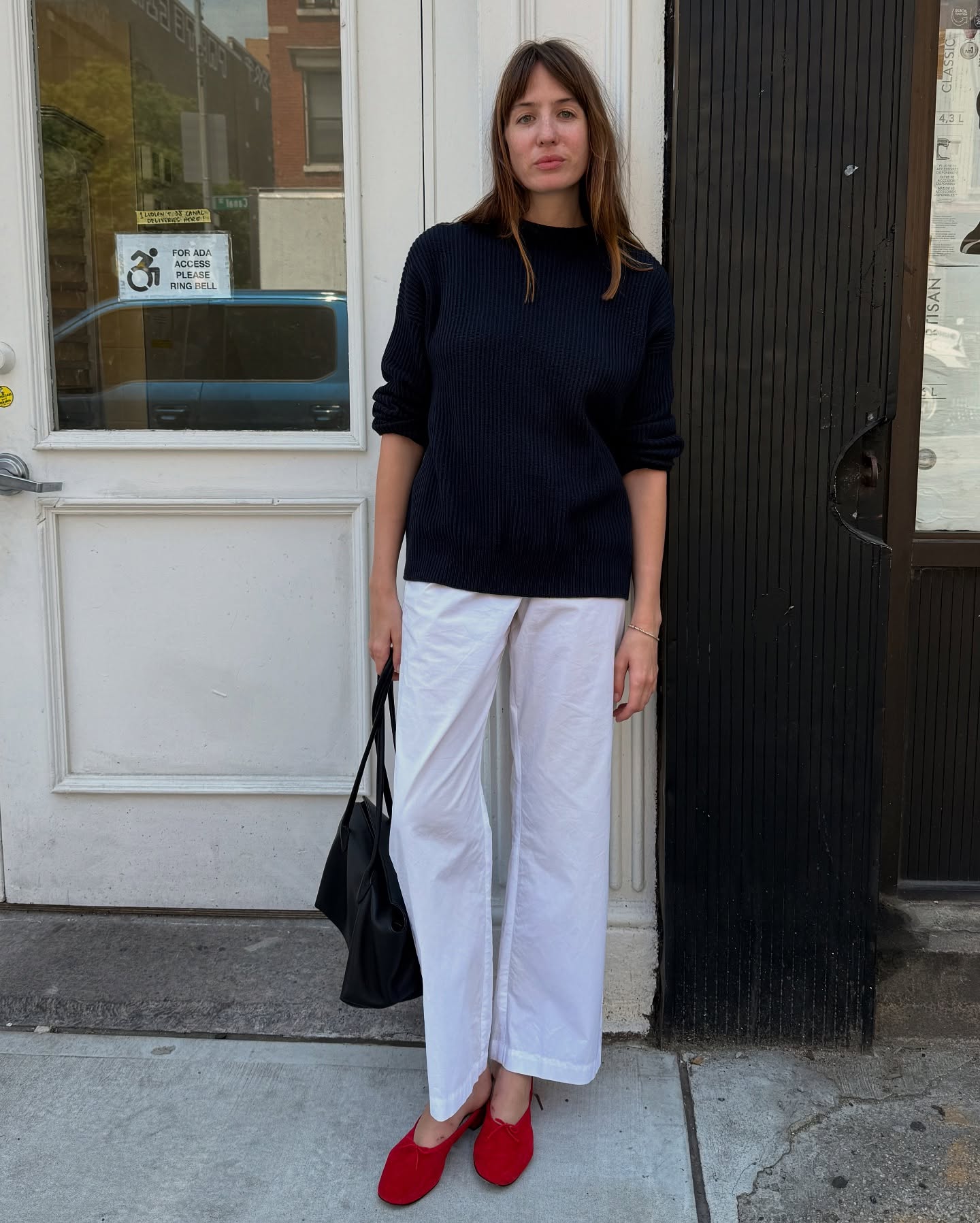 An image of @lizzyhadfield wearing a black sweater, white cotton pants and red slippers while in New York.