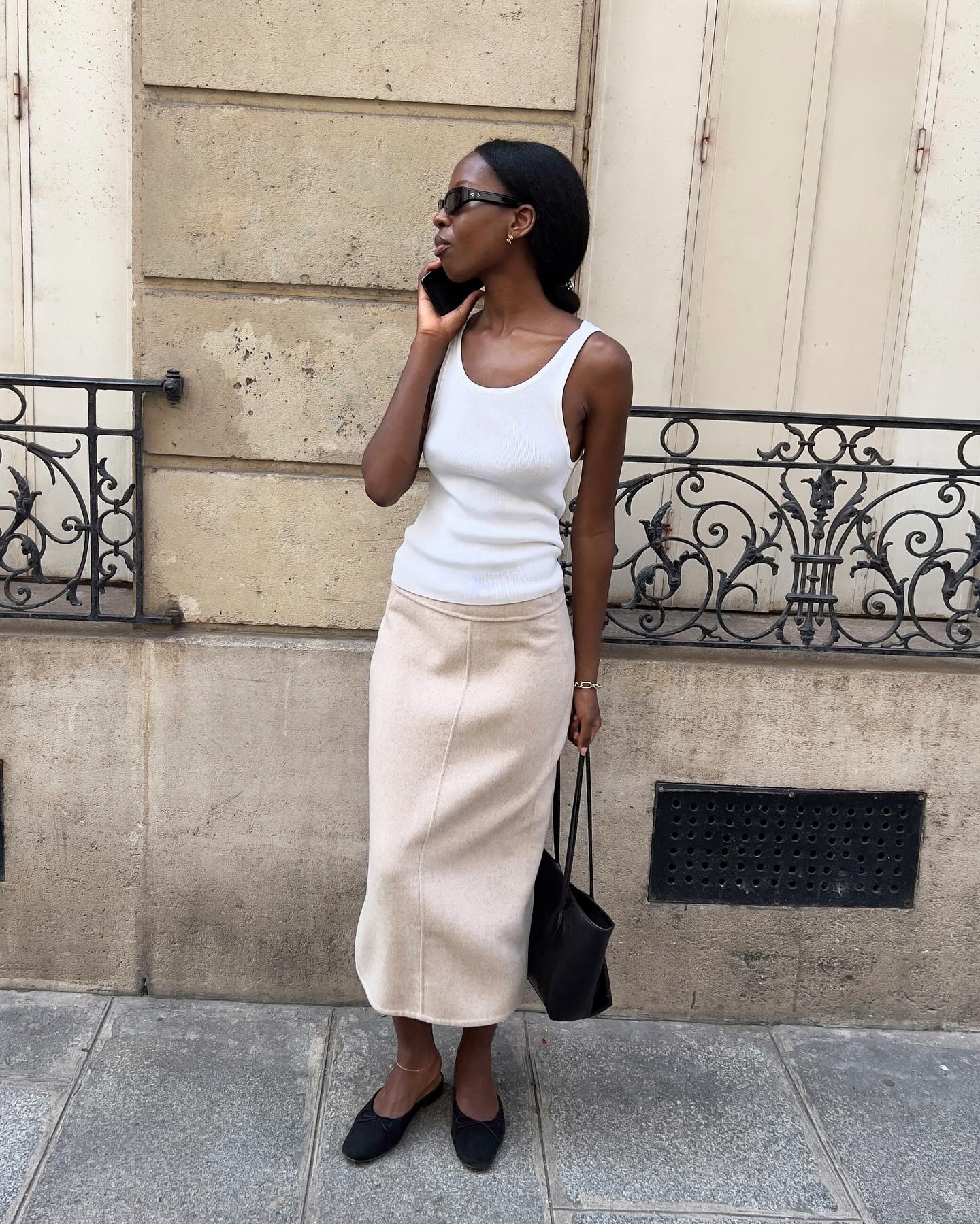 Influencer wears black suede mules with a longline cream skirt and a white tank top.