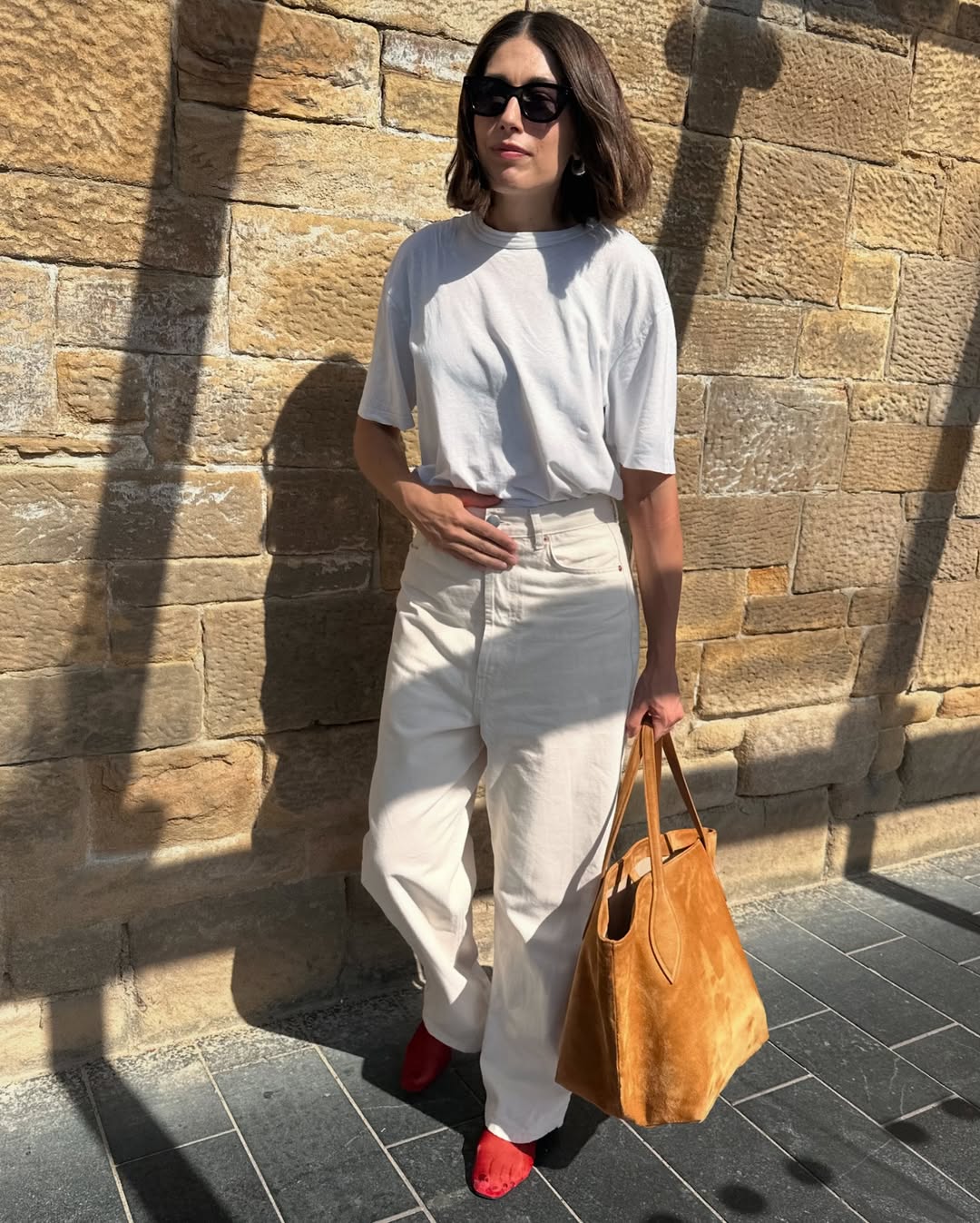 @lucyalston_ wears red mesh flats with ecru jeans, a white t-shirt and tan suede tote bag