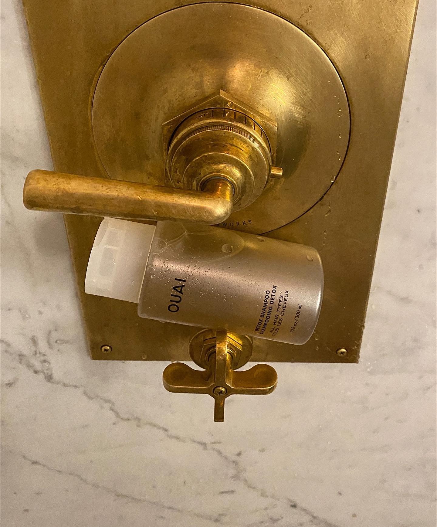 A Ouai shampoo bottle in a gold and marble shower