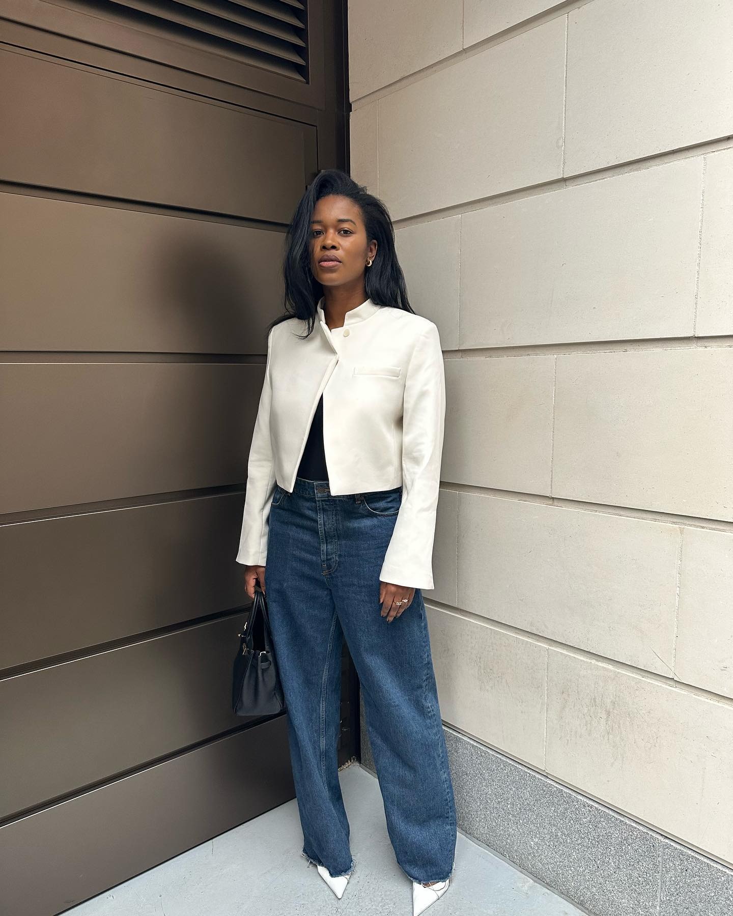 Influencer @nlmarilyn stands outside wearing a white jacket, wide-leg jeans and pointed-toe heels.