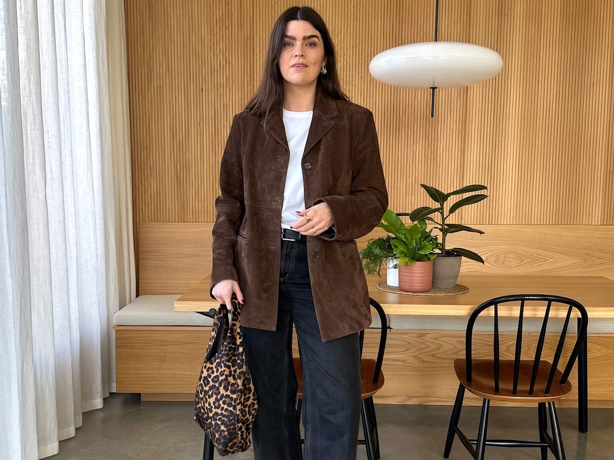 British style influencer Anna Newton poses in her chic London dining room wearing a brown suede jacket, white T-shirt, black belt, black jeans, and a leopard-print bag