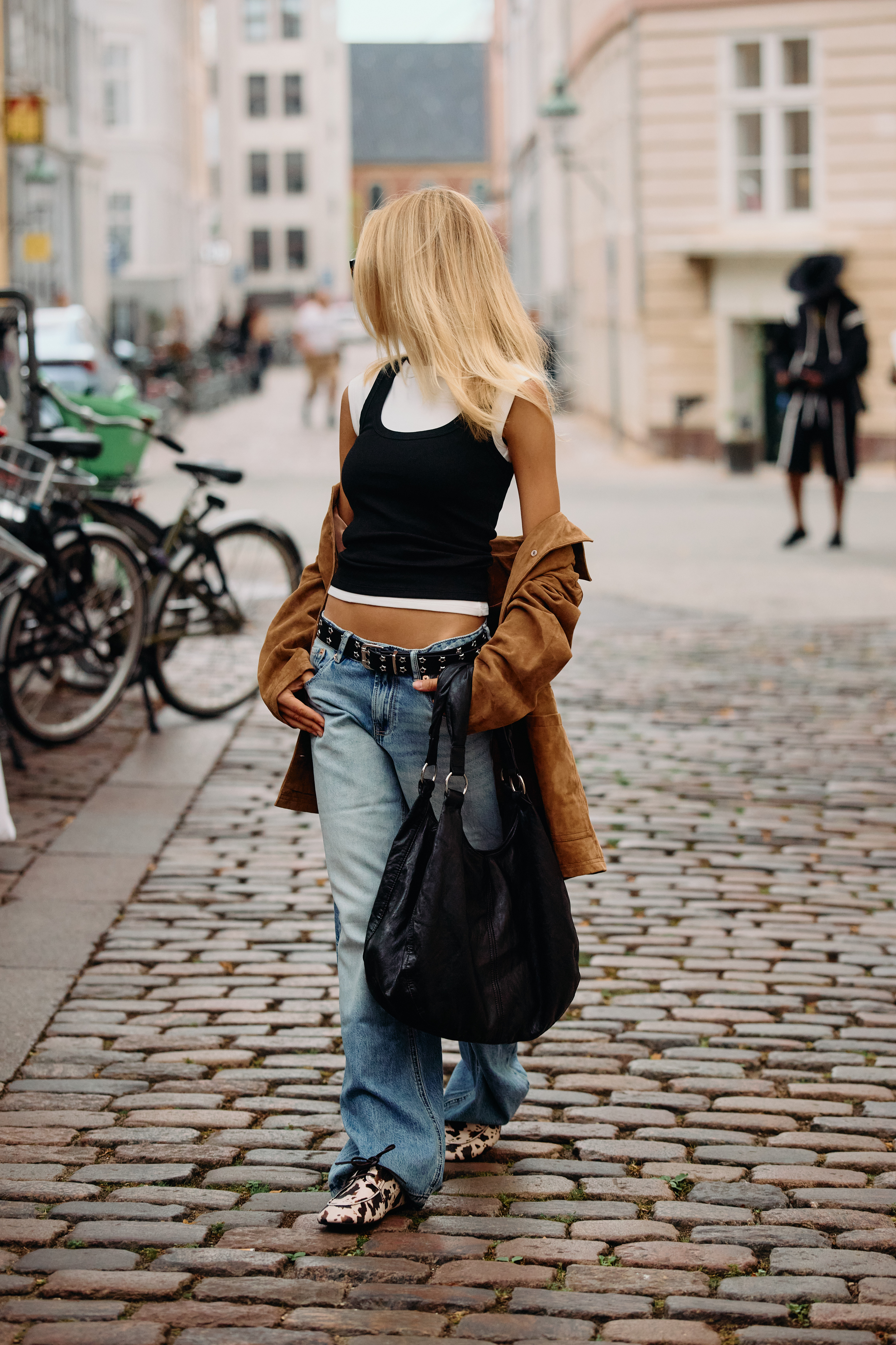 Fashion Week attendee wears leopard print loafers with low-rise baggy jeans and a vest top layered over a white tee.