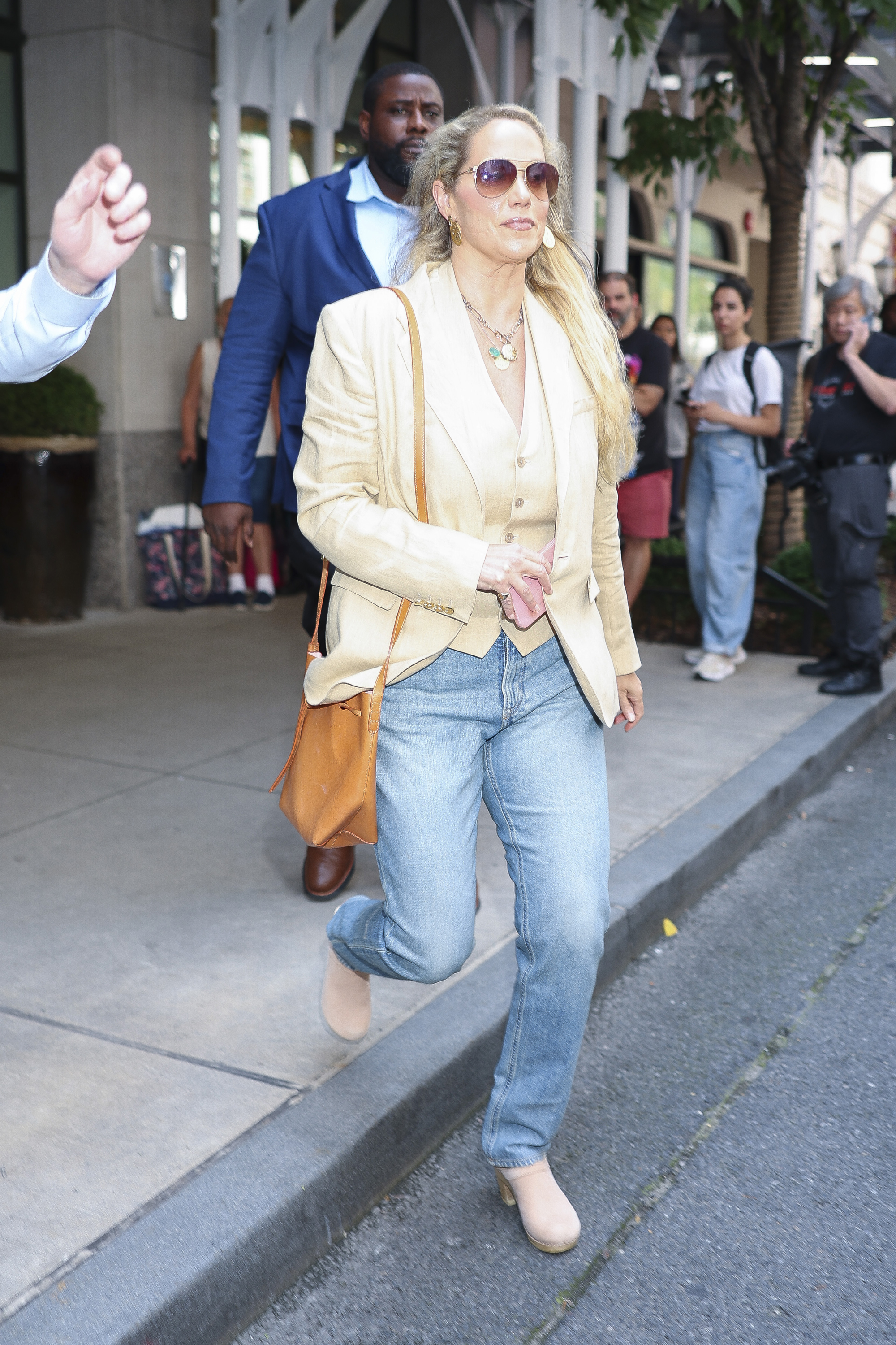 Elizabeth Berkley was seen in NYC wearing suede clogs, a beige blazer, and a vest with light wash jeans.