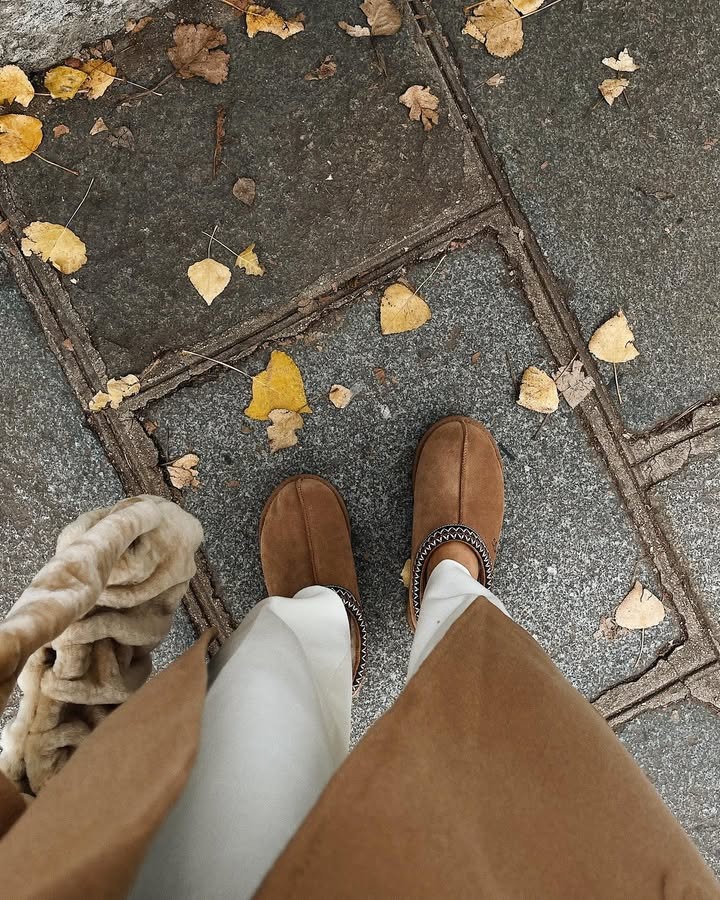 Influencer Julia wears Ugg clogs with white pants and a brown coat.