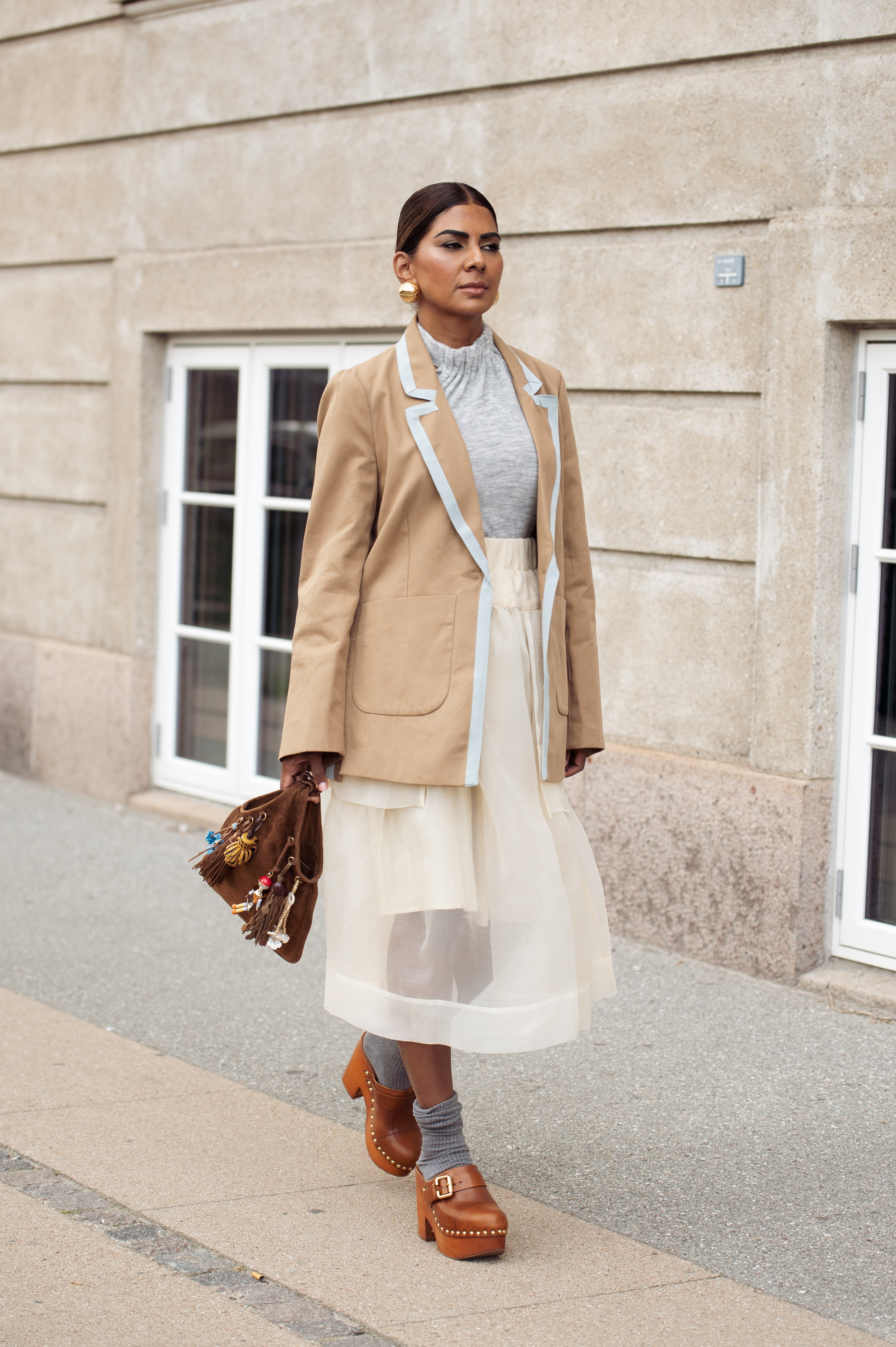 Zufi Alexander at Copenhagen Fashion Week August 2025 wearing a white sheer skirt, grey top, brown suede blazer, and leather clog mules.