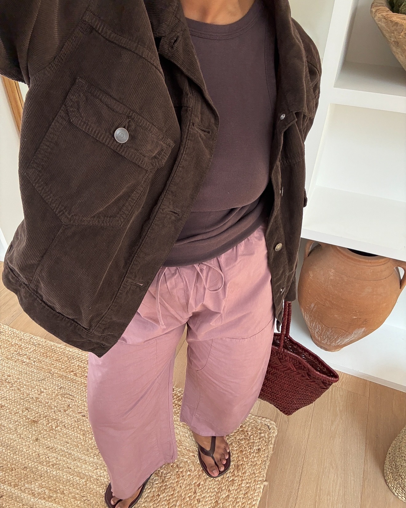 Influencer @monikh wears a chocolate brown vest top with pink linen trousers and black flip-flops.