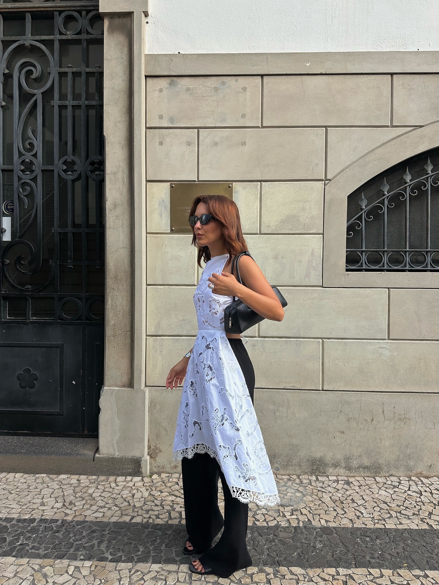 Influencer @deborabrosa wears a white long time crochet detail top over black trousers with black heeled sandals.