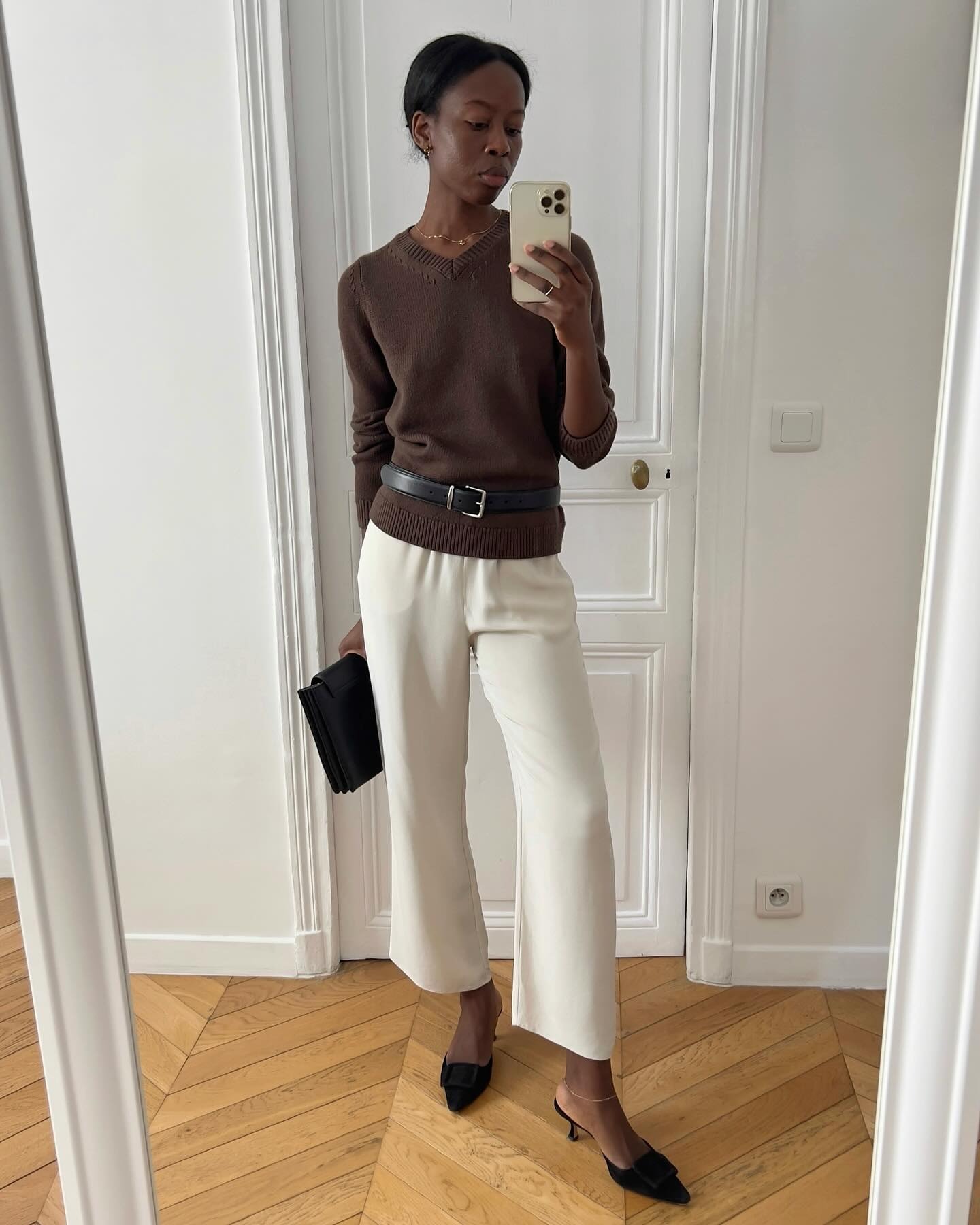 @sylviemus_ wearing a brown V-neck sweater and cream pants.