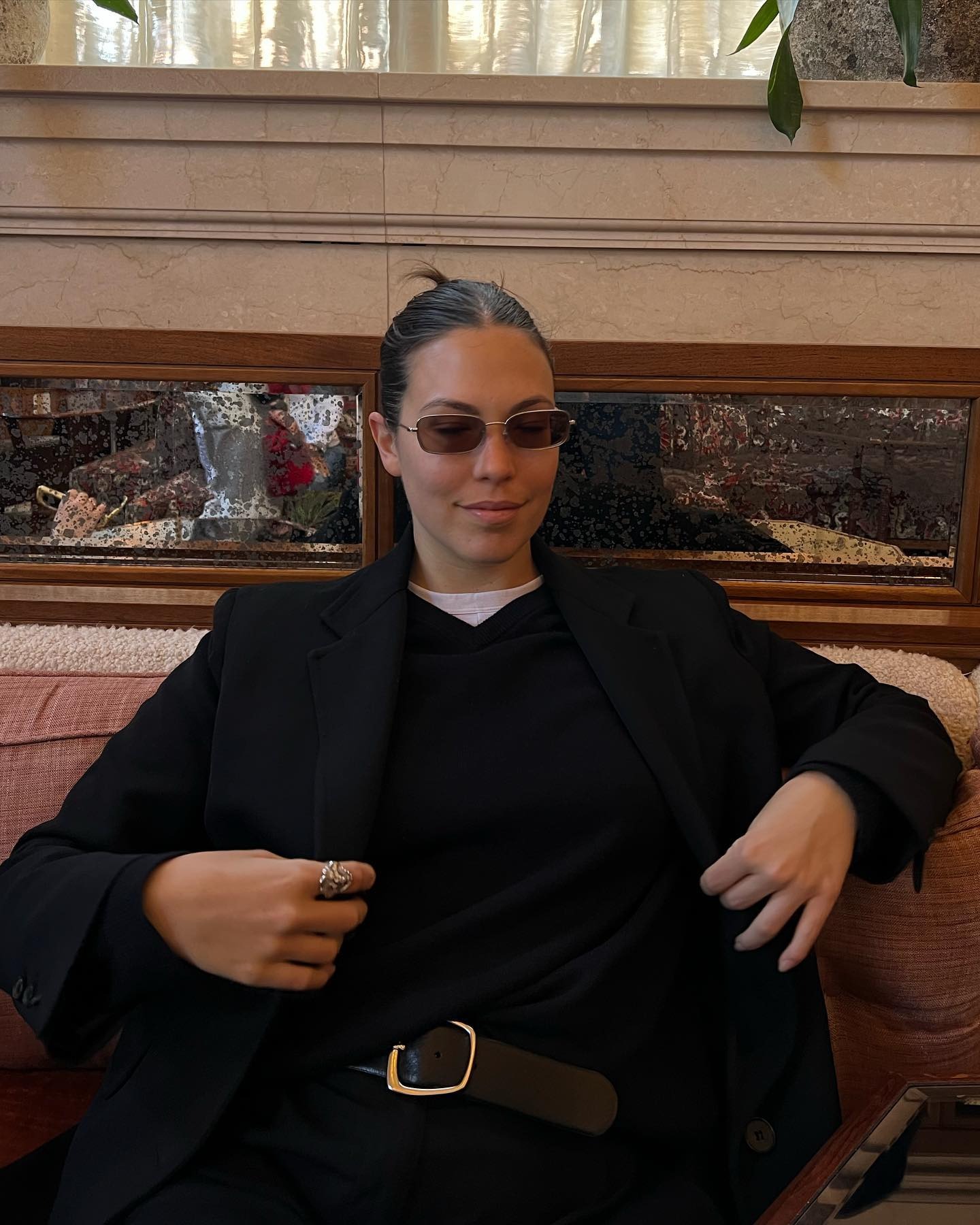 @rachelbesser wearing a white T-shirt, black V-neck sweater, and black pants.