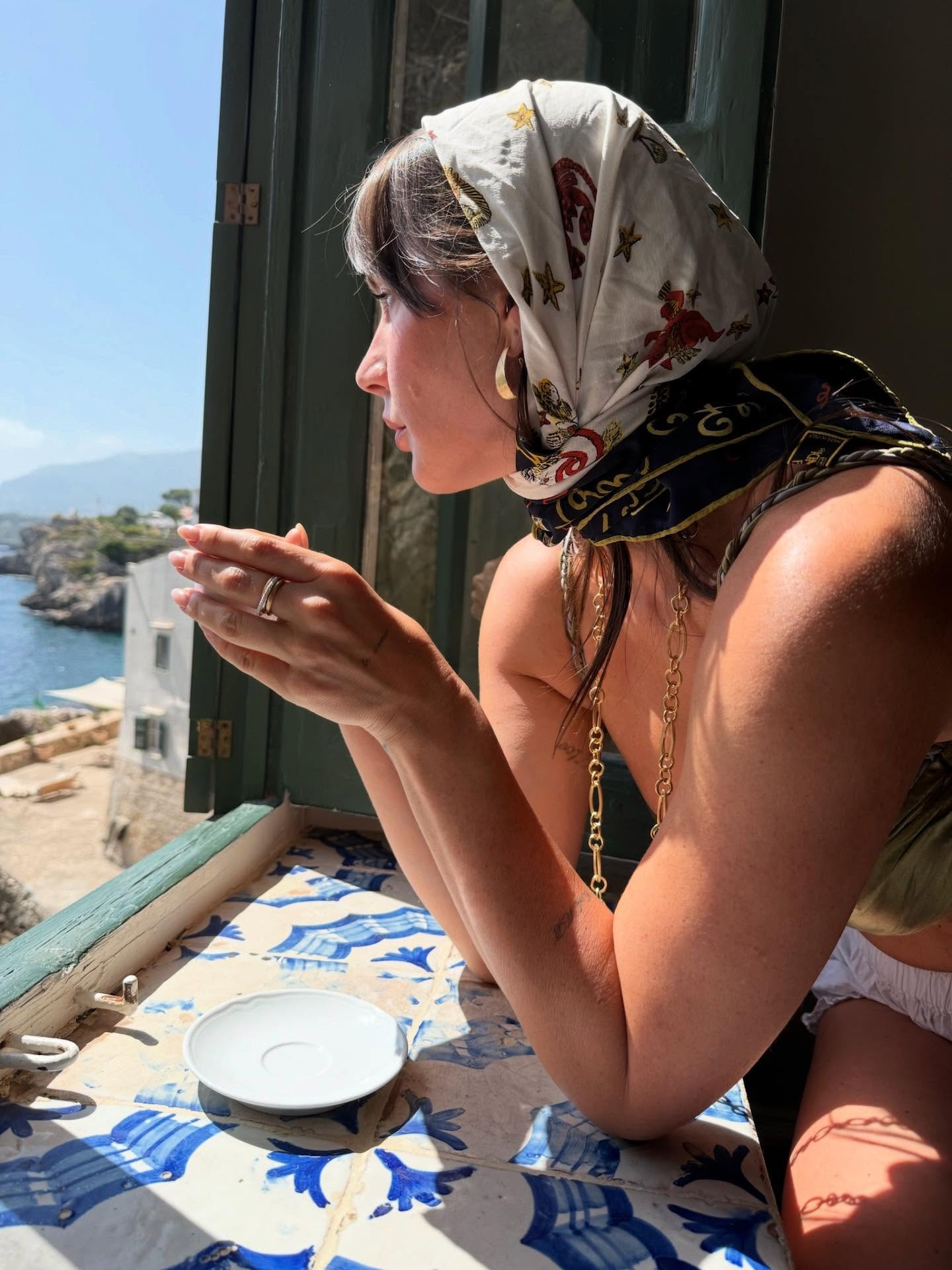 Woman wearing silk scarf, sitting on European windowsill.