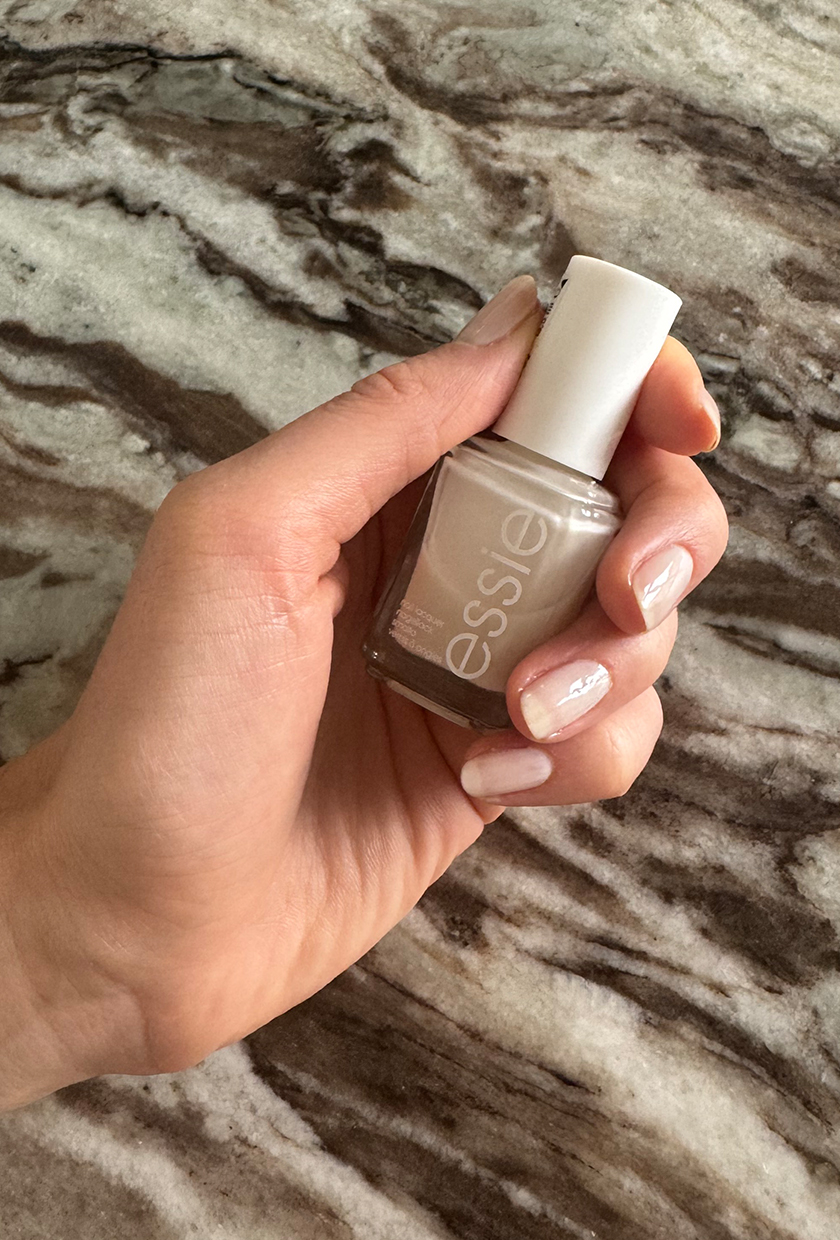 Eleanor's hand holding a bottle of Essie Allure nail polish