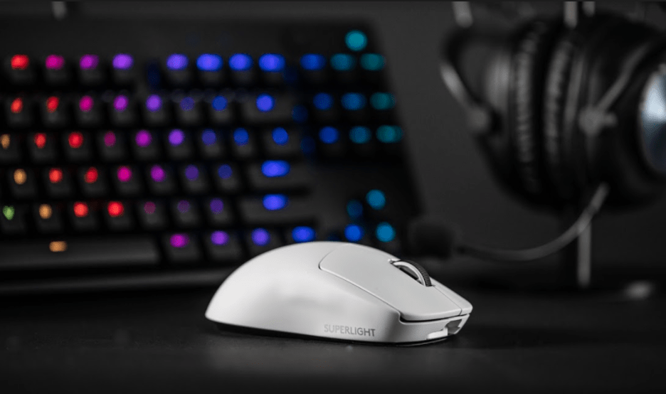 A close-up image of Logitech’s white G Pro X Superlight mouse in front of a headset and an RGB keyboard.