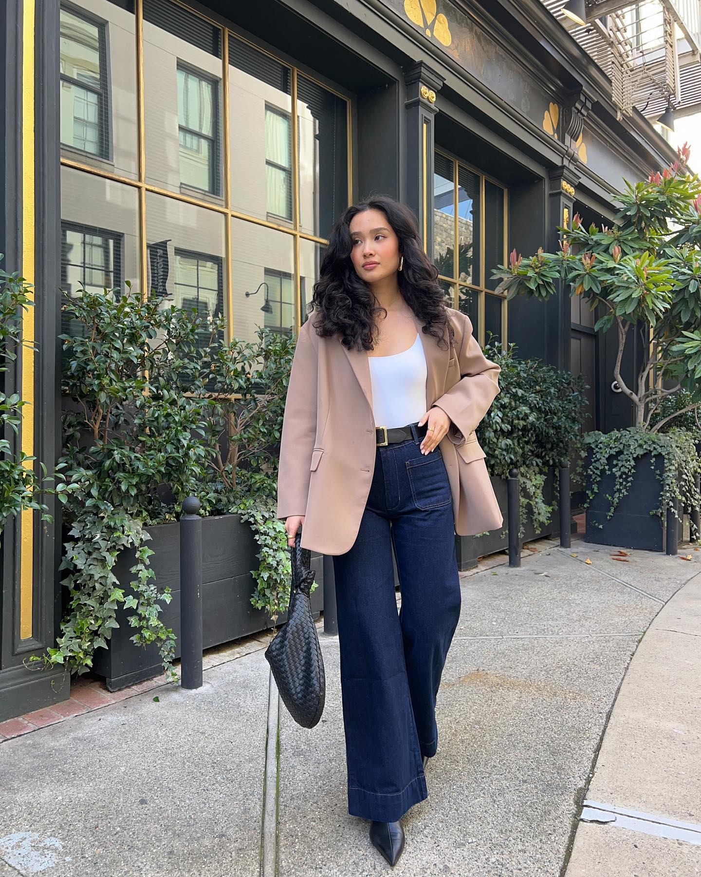 Influencer @kristincabat wears dark wash flared jeans with pointed toe boots and a camel blazer.