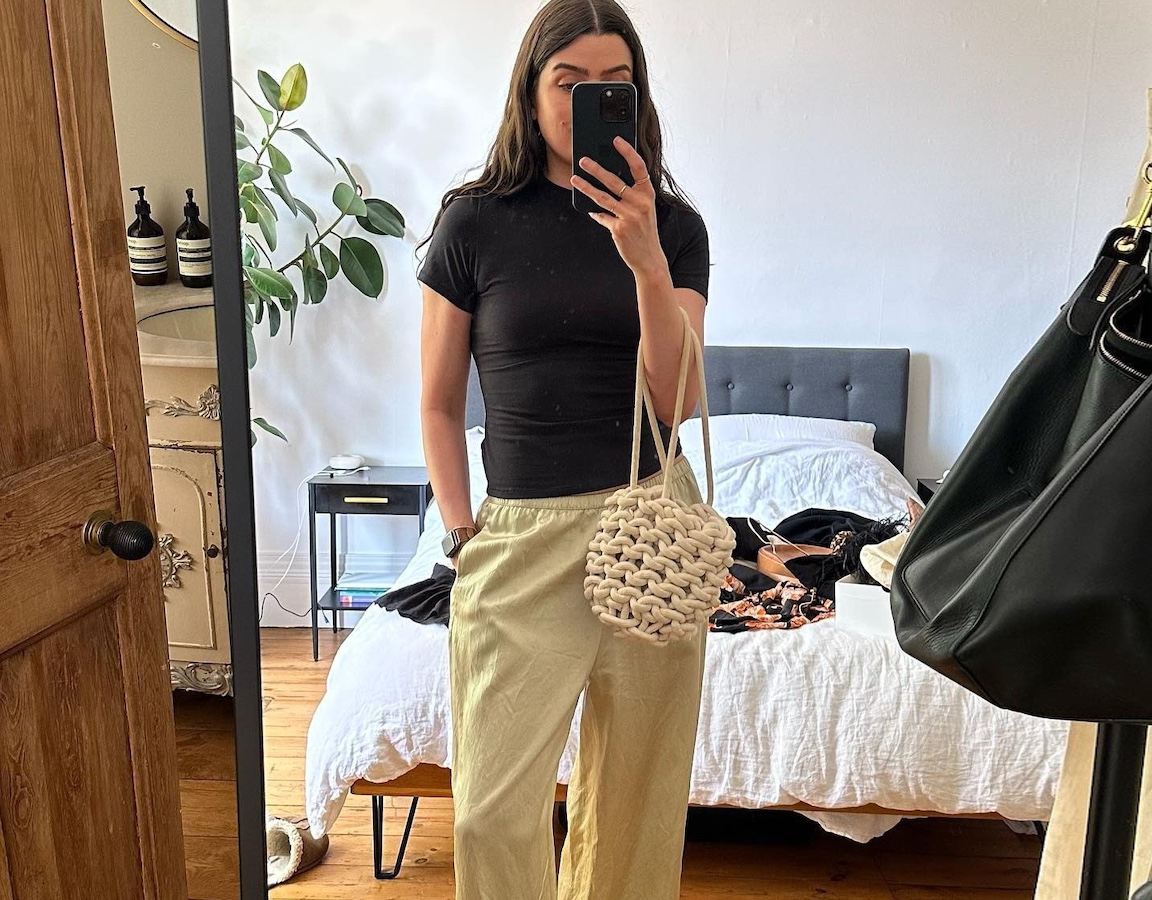 British style influencer Anna Newton poses for a mirror selfie wearing a black t-shirt, knotted bag, and pull-on satin pants