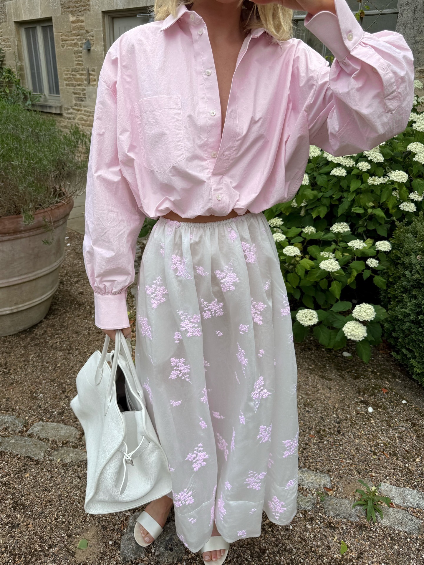 Model Elsa Hosk carries a white leather handbag, wearing a pink skirt, a white floral skirt and white strappy sandals.