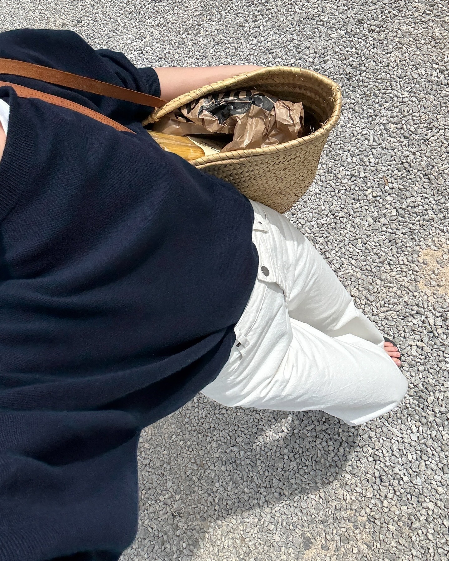 Influencer @claradyrhauge wears a navy jumper with white jeans, sandals and a wicker bag.