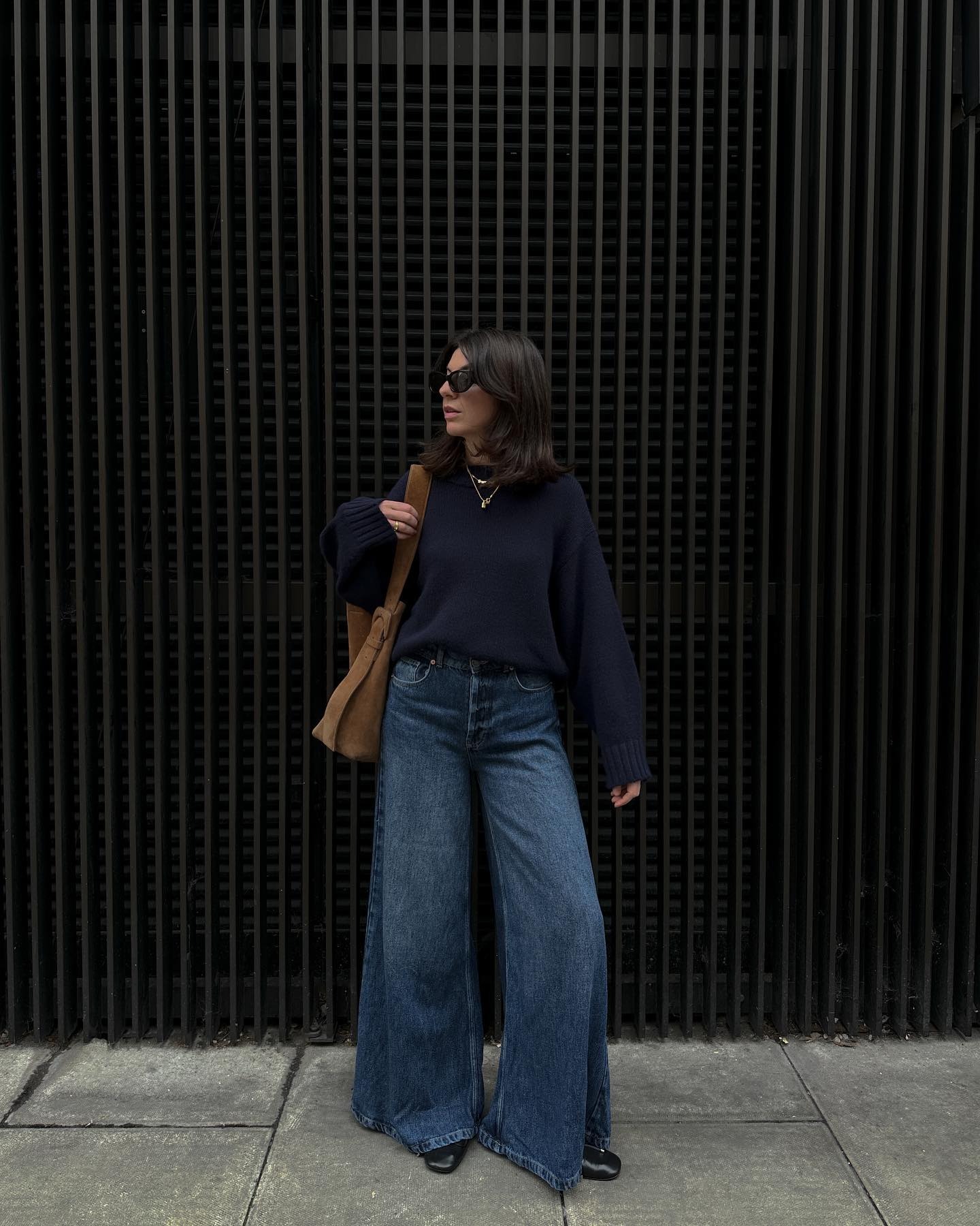 Influencer @francescasaffari stands in front of a black wall wearing. navy knit with dark wash jeans.