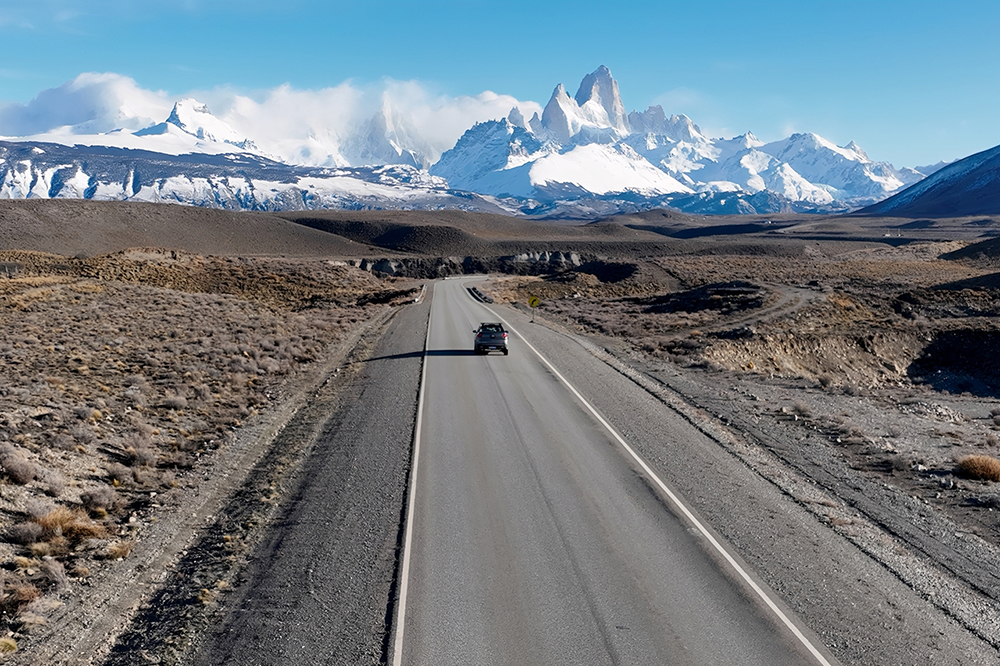 A car drives along a road in patagonia towards snowy mountains