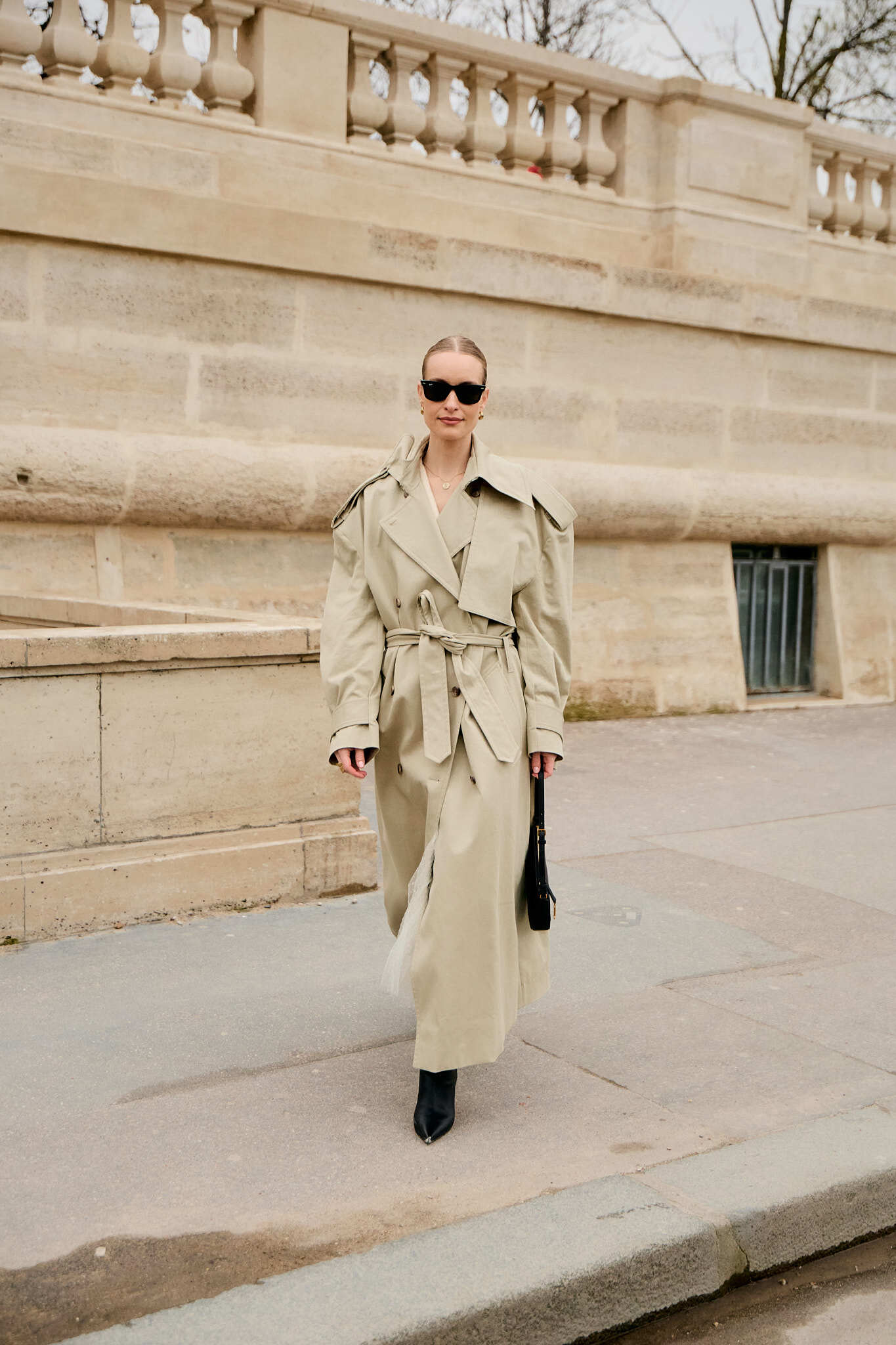 A woman wears a long trench coat and black boots.