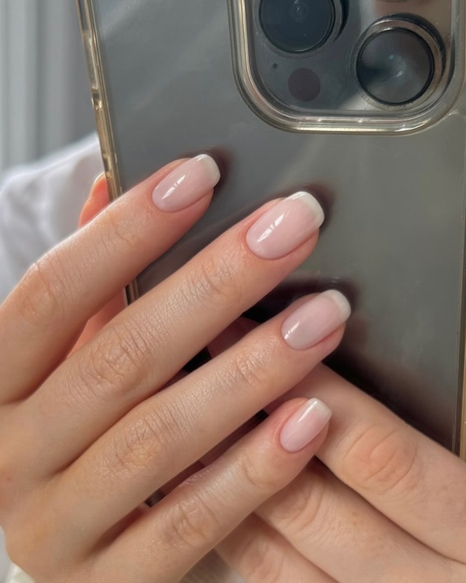 A woman taking a mirror selfie of her blurred French manicure