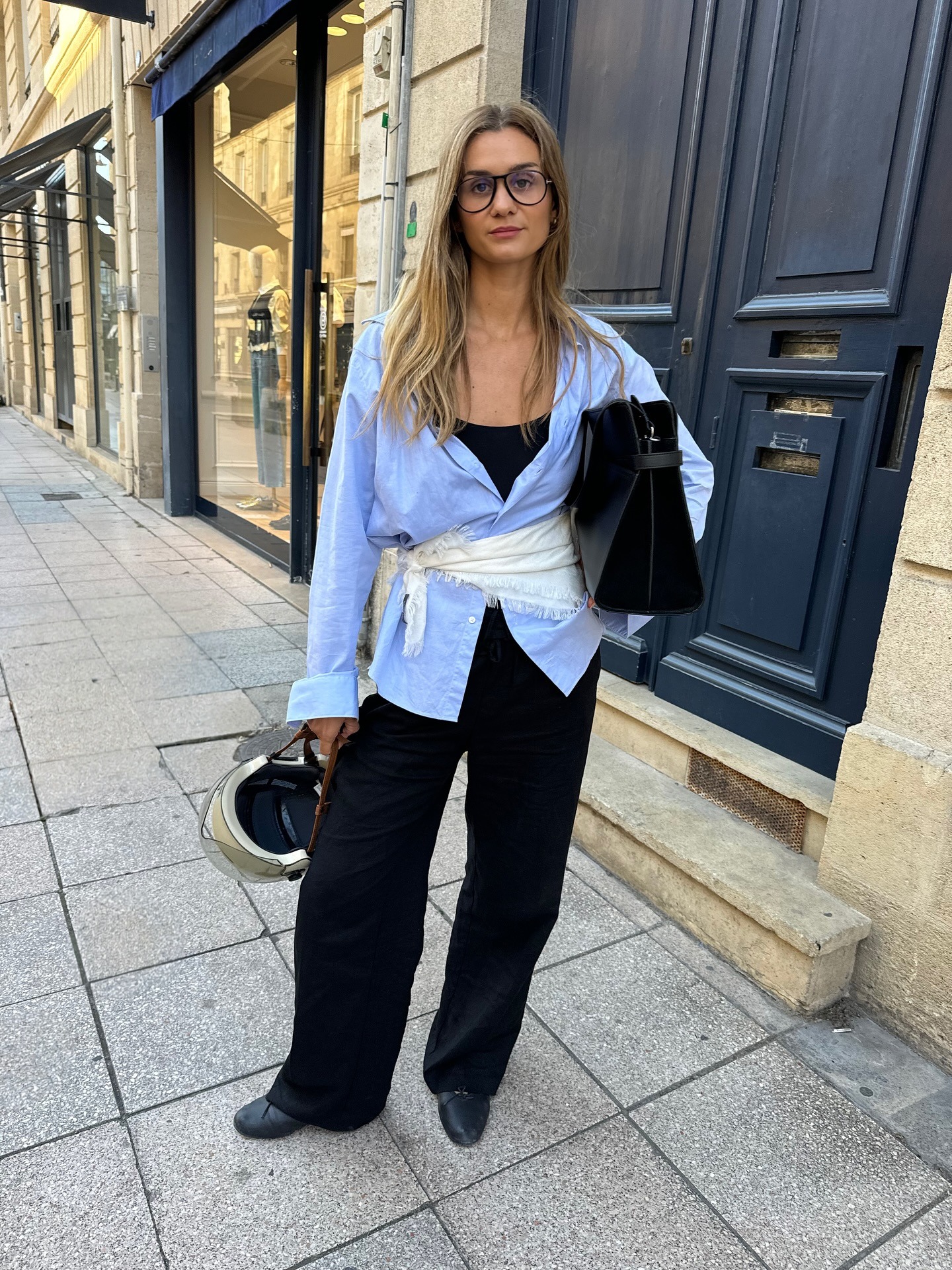 Influencer @annelauremais wears black leather ballet flats with a blue shirt, black trousers and white scarf tied around her waist.