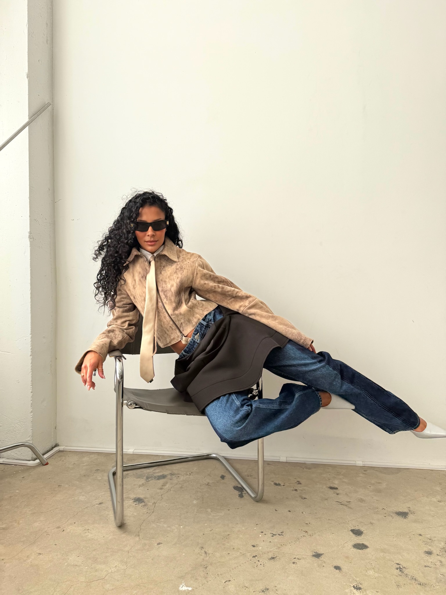 sami wears a leather jacket, tie, skirt, and blue jeans.