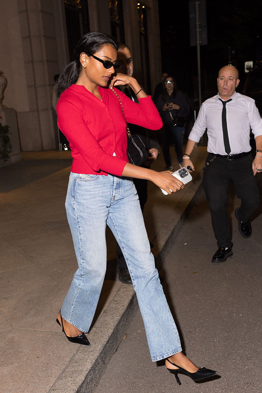 Simone Ashley wearing a red cardigan, blue jeans, and black Prada heels