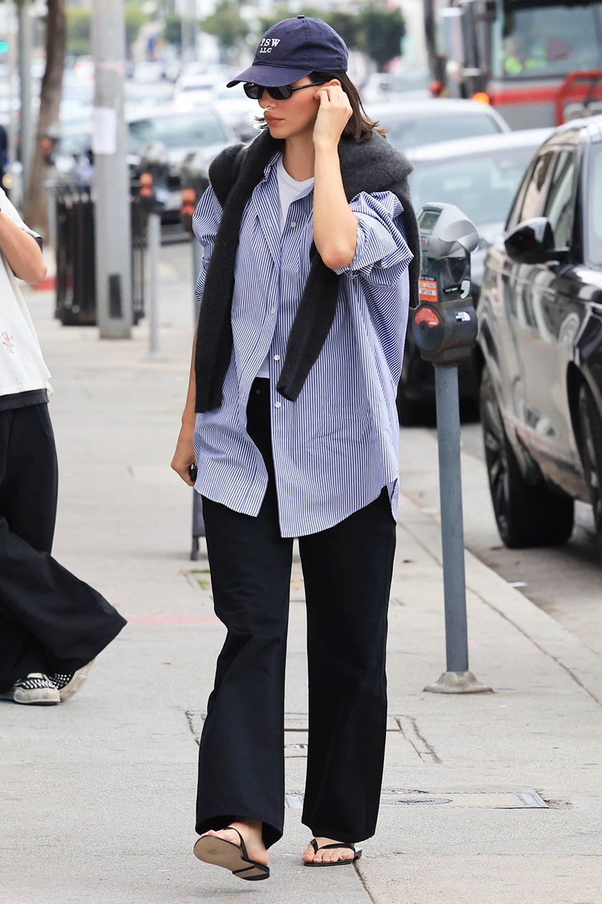 Kendall Jenner wearing a striped button-down shirt with a sweater draped over her shoulders, loose black pants, and flip-flops in L.A.