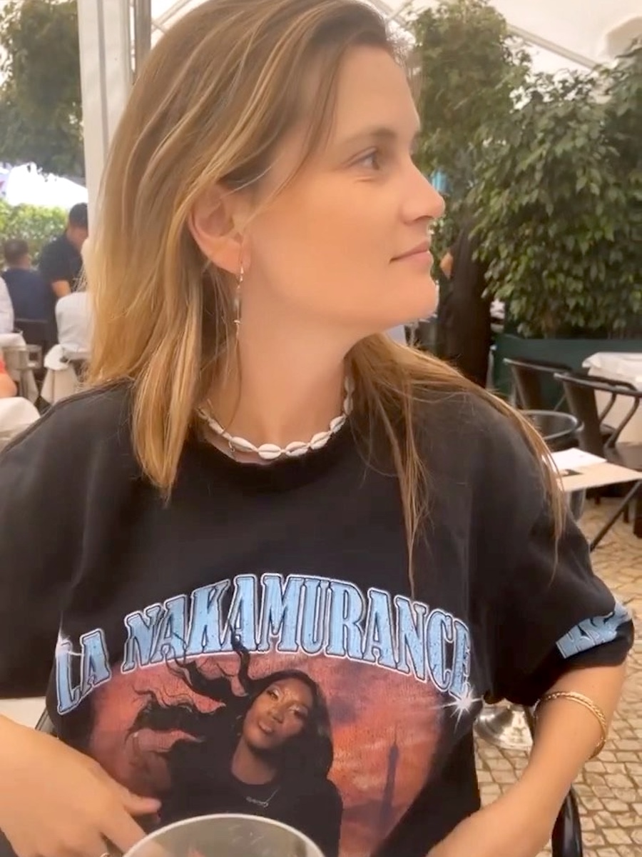 French writer, editor, and creative Eugenie Trochu sits at a cafe wearing a vintage-inspired tee from Aya Nakamura and Balenciaga along with a shell necklace