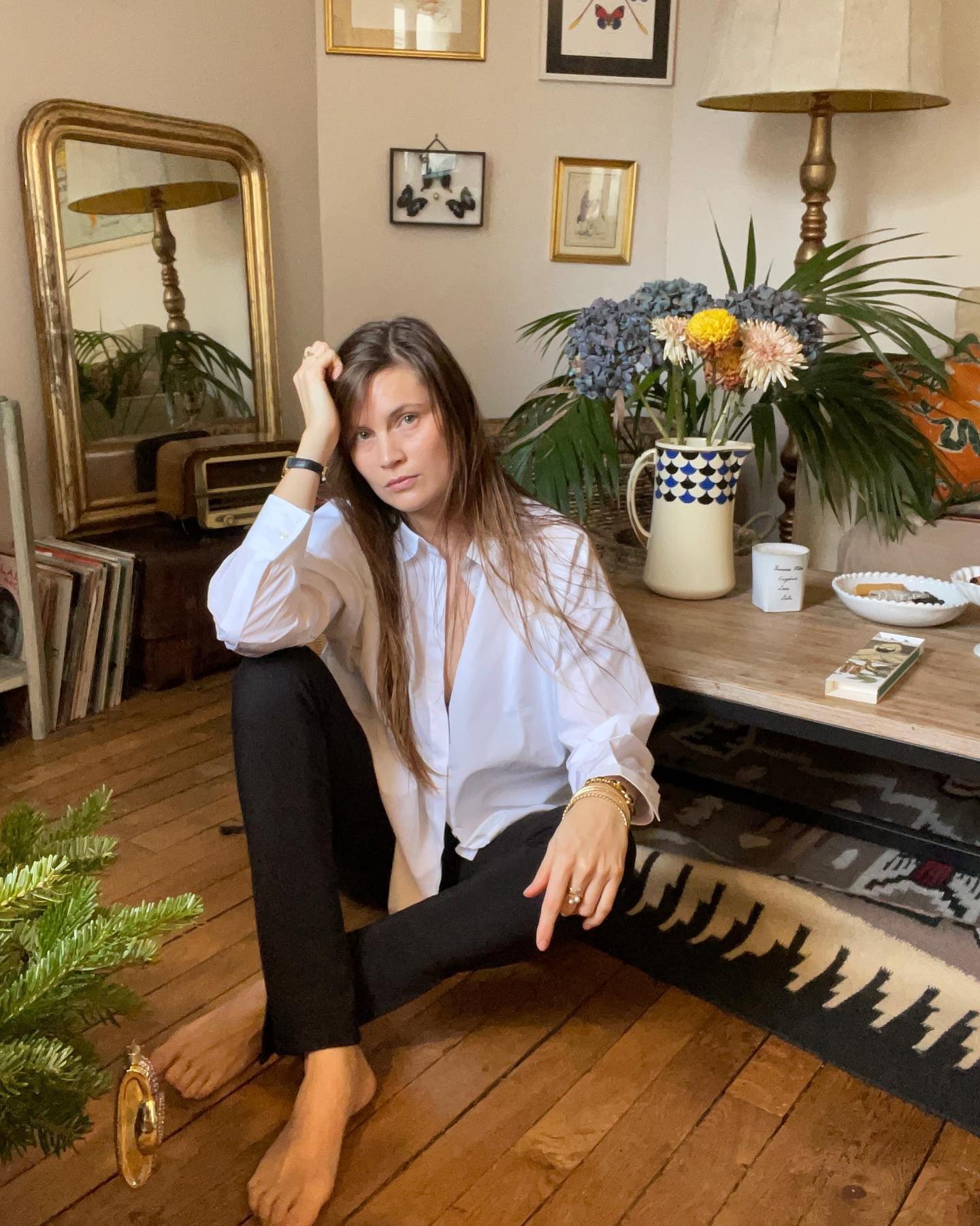 writer, editor, and creative Eugenie Trochu poses in a Paris apartment wearing a white button-down shirt, and chic black pants