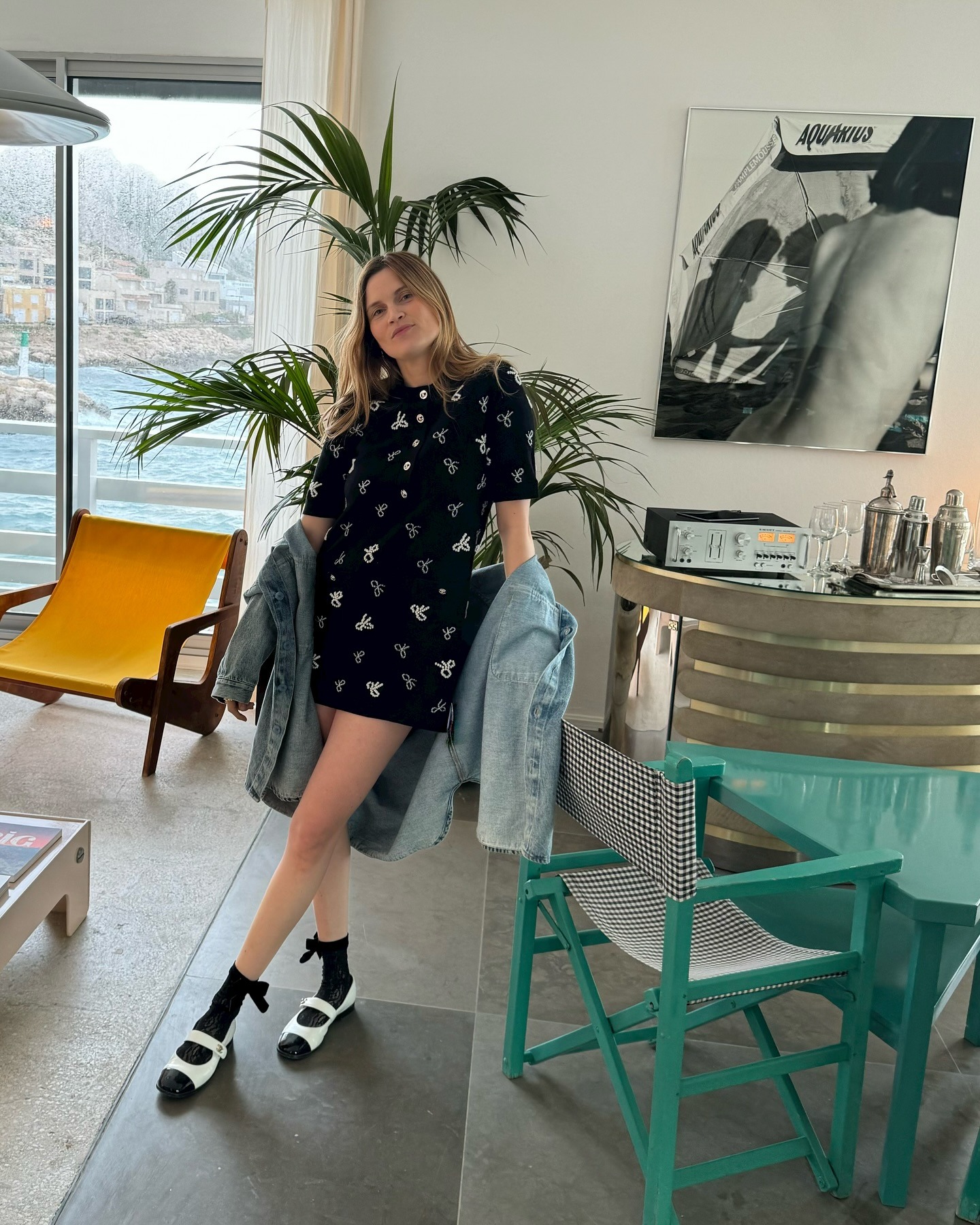 French writer, editor, and creative Eugenie Trochu poses in Marseille, France wearing a black and white printed mini dress, a denim shirt, ankle bow socks, and cap-toe Mary Jane flats