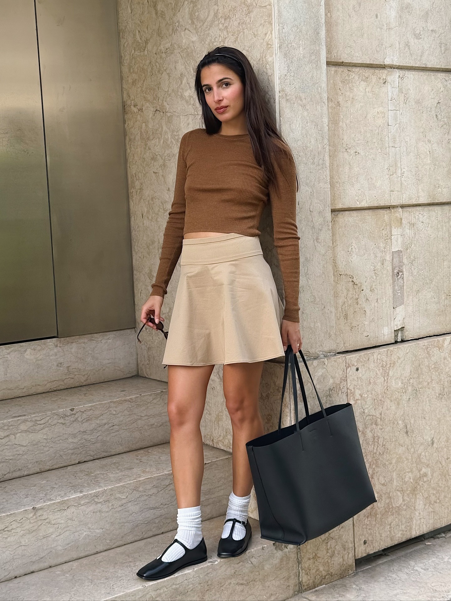 Influencer @tamaramory wears black t-bar flats with a beige skirt and brown knit.