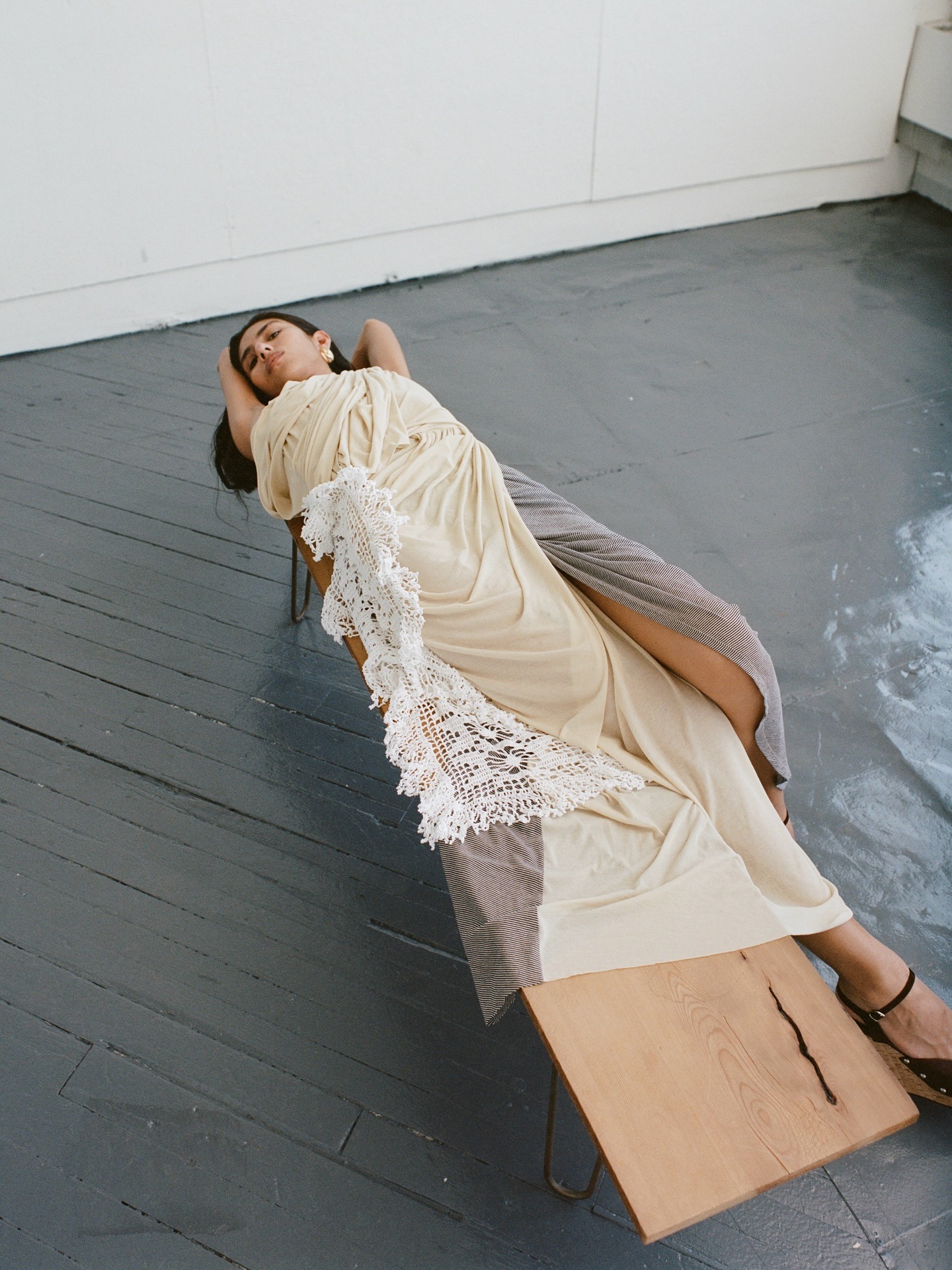 A woman lays on a bench wearing a butter yellow dress with lace details.